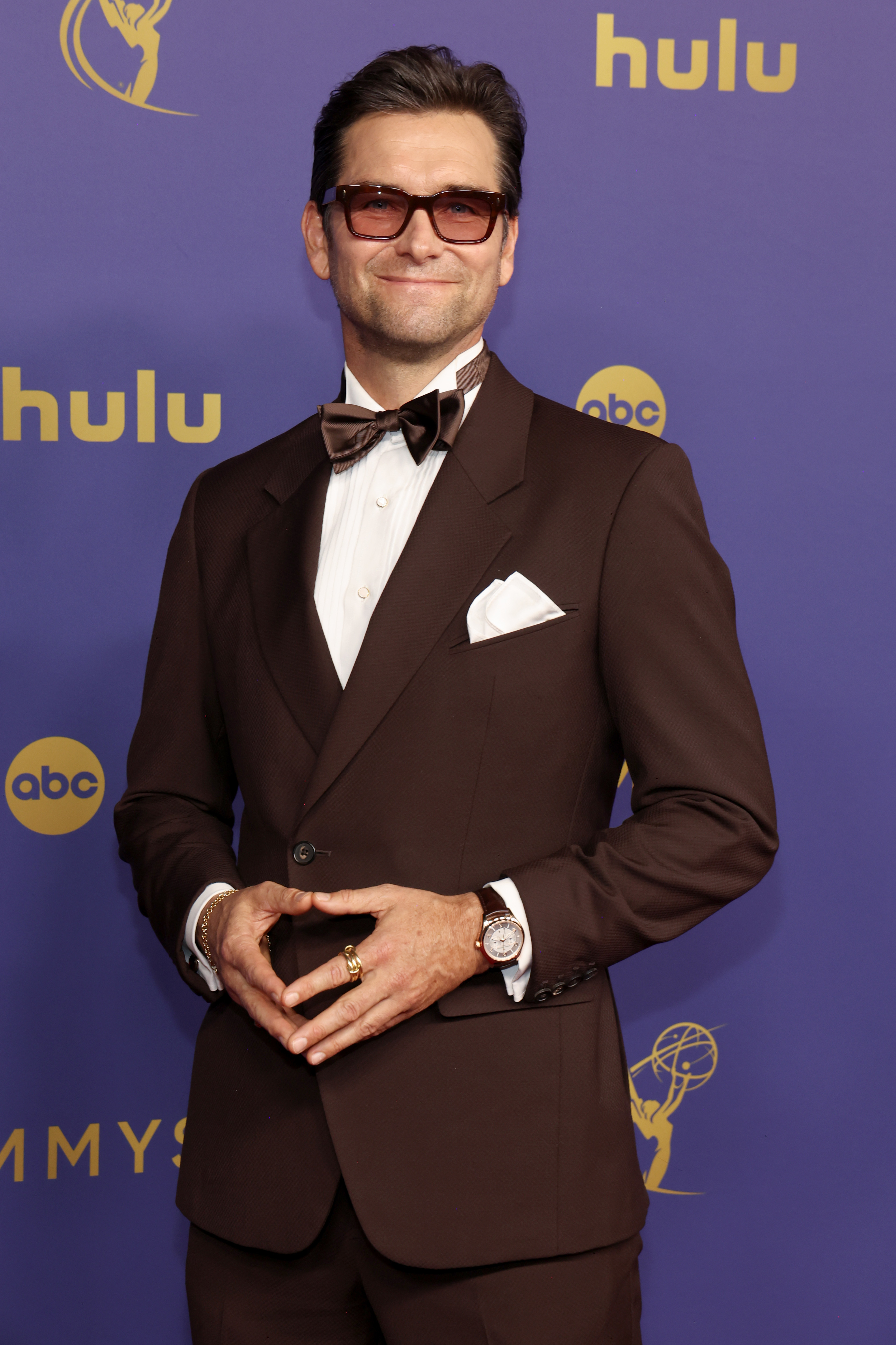 Antony Starr in a tuxedo with a bow tie and sunglasses poses on the red carpet at the 2024 Emmys