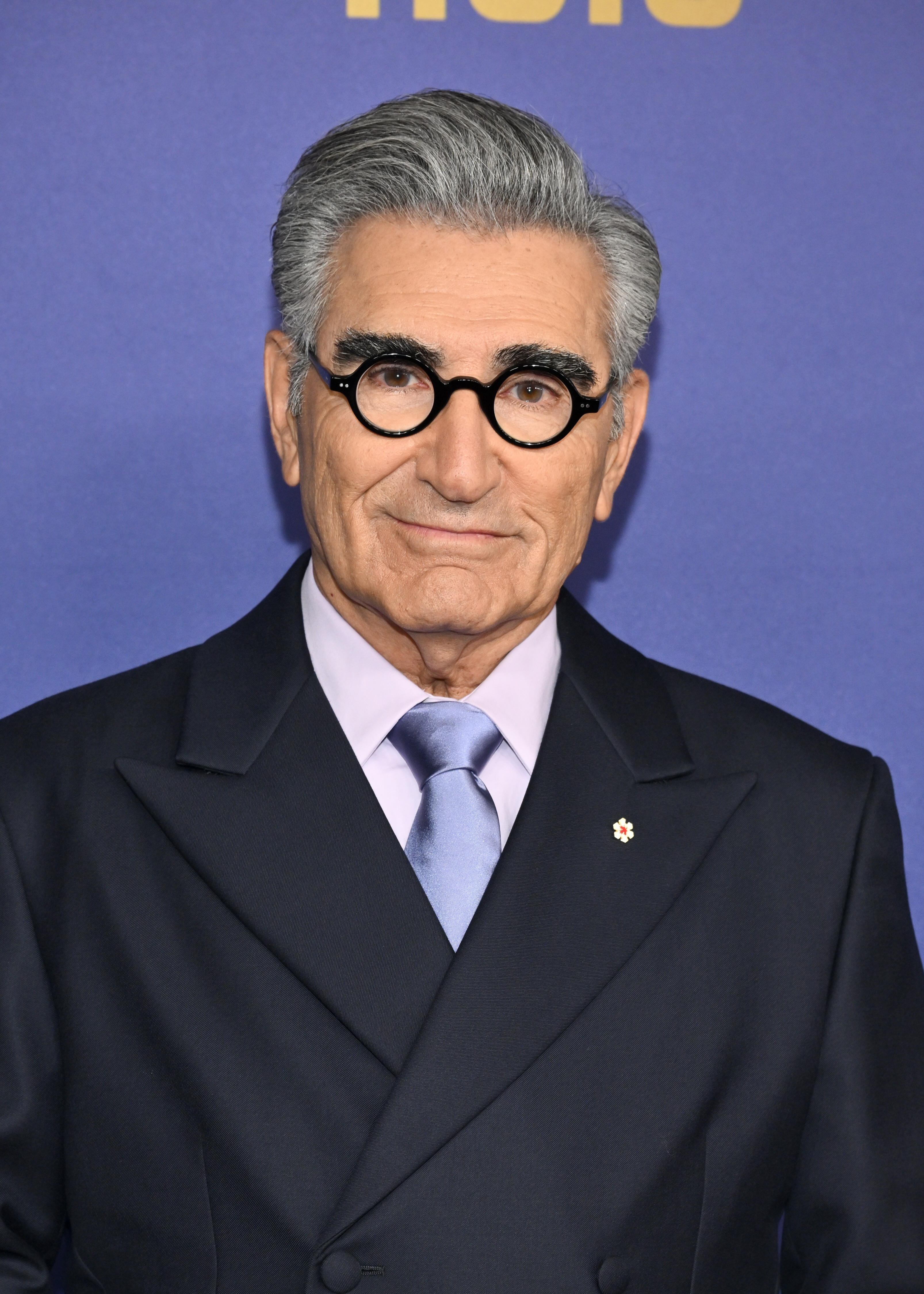 Eugene Levy in a formal suit and tie, posing for a photo