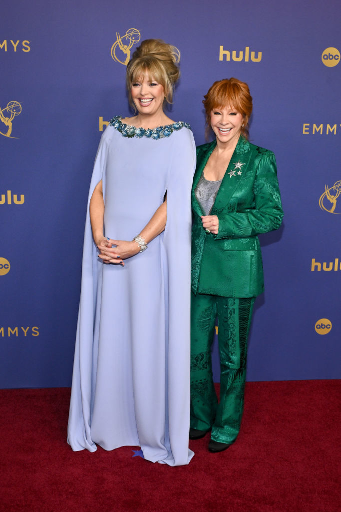Rita Wilson in a light gown with floral details and Reba McEntire in an emerald green suit on the red carpet at the Emmys