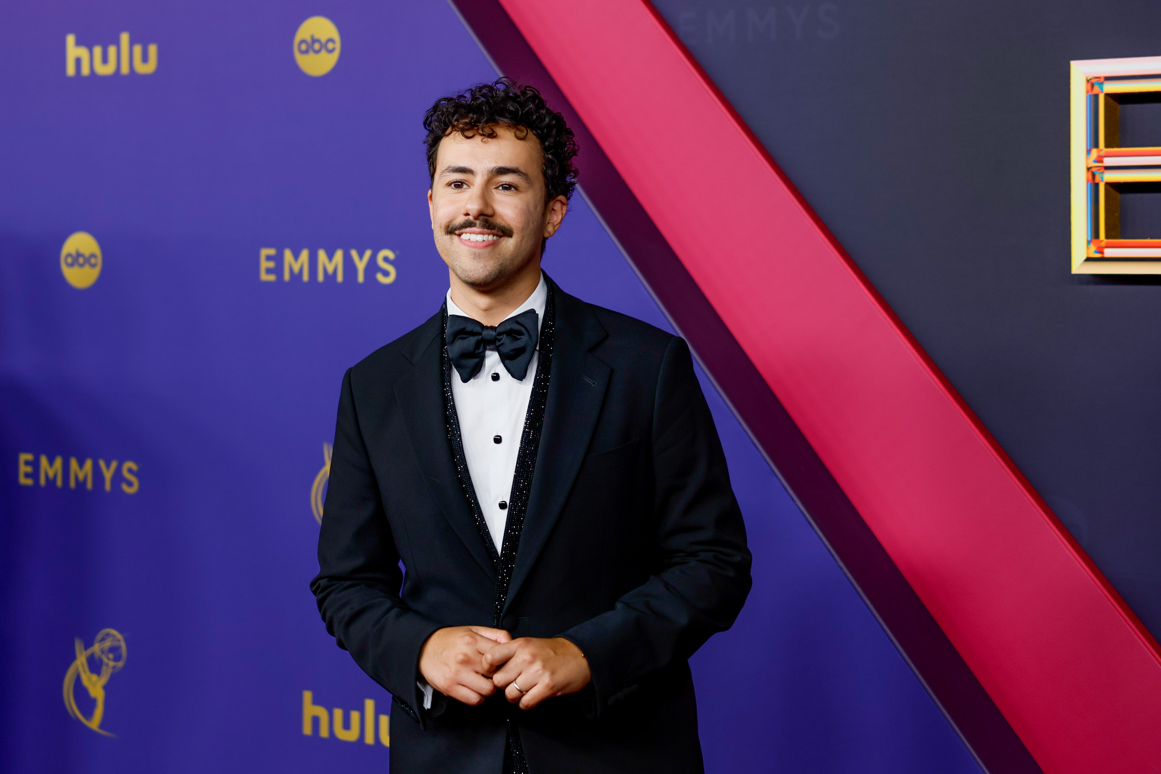 Ramy Youssef on the red carpet at the Emmys, wearing a classic tuxedo with a bow tie