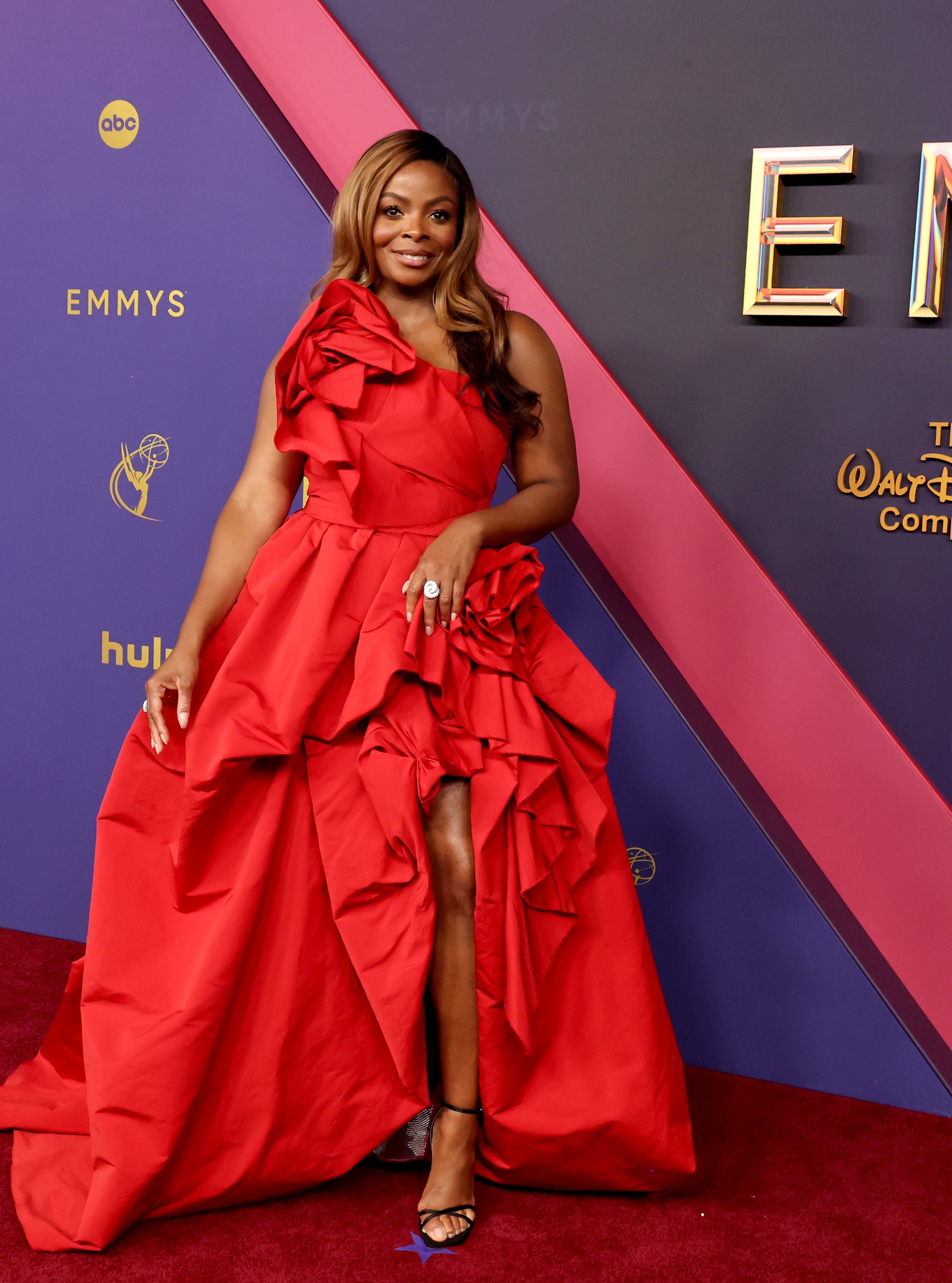 Janelle James poses in a flowing, ruffled, red gown on the red carpet at the Emmys event