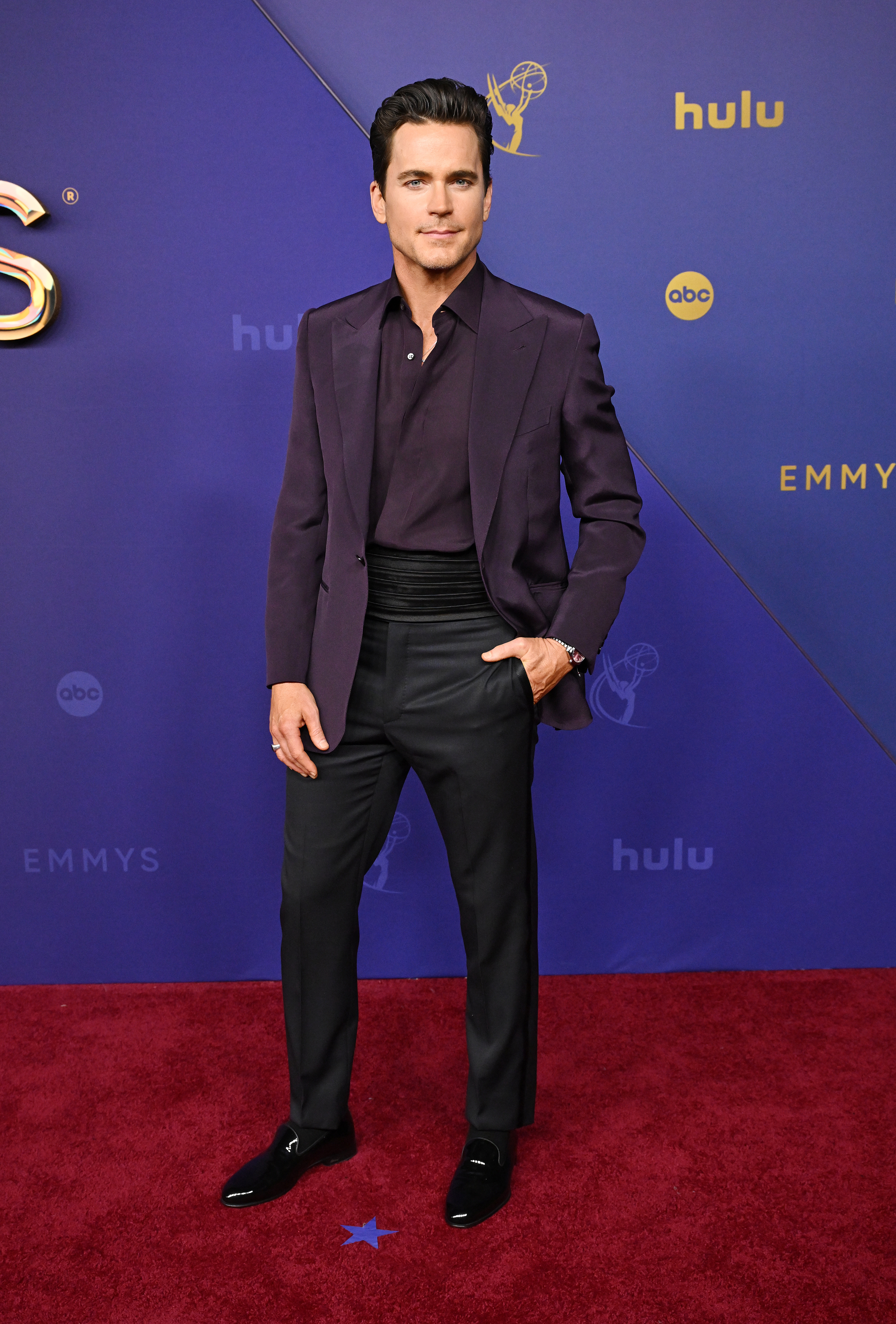 Matt Bomer on the red carpet in a dark suit jacket, shirt, trousers, and shoes, attending the Emmys