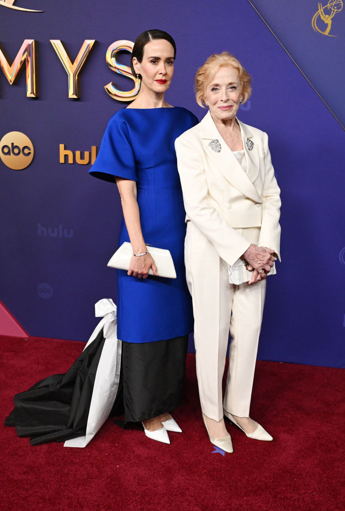 Sarah Paulson in a stylish blue gown with a black and white train, and Holland Taylor in a chic white suit, pose on the red carpet at the Emmys