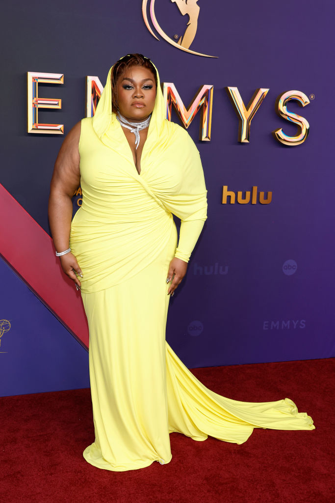 Nicole Byer in a floor-length, hooded yellow gown, posing on the red carpet at the Emmys