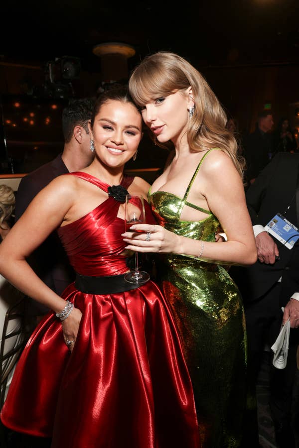 Selena Gomez in a satin gown and Taylor Swift in a shiny dress pose together at a social event
