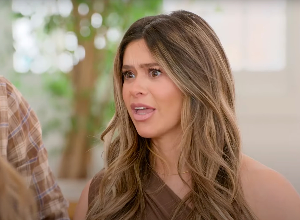 Taylor Frankie Paul with long hair looks surprised, wearing a sleeveless top, with blurred greenery in the background