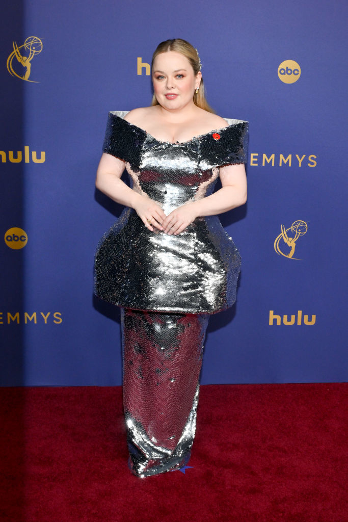Nicola Coughlan on the red carpet, wearing a shiny, metallic, structured dress at the Emmys