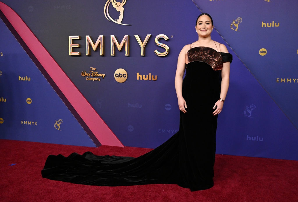 Lily Gladstone on the red carpet at the Emmys, wearing an elegant off-shoulder gown with a long train and a breast plate