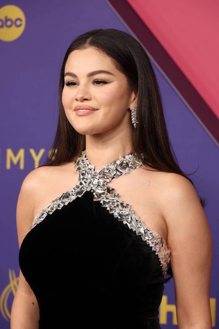 Selena Gomez on the red carpet wearing a sleek black dress with intricate silver detailing around the neckline and shoulders