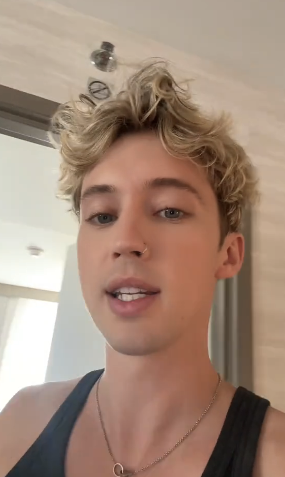 Troye Sivan selfie, short blond curly hair, wearing a tank top and a necklace with a small pendant