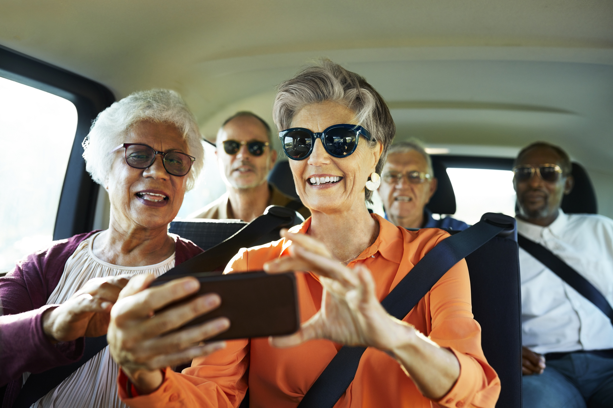 Smiling woman using smart phone by friend in car; older friends are traveling together