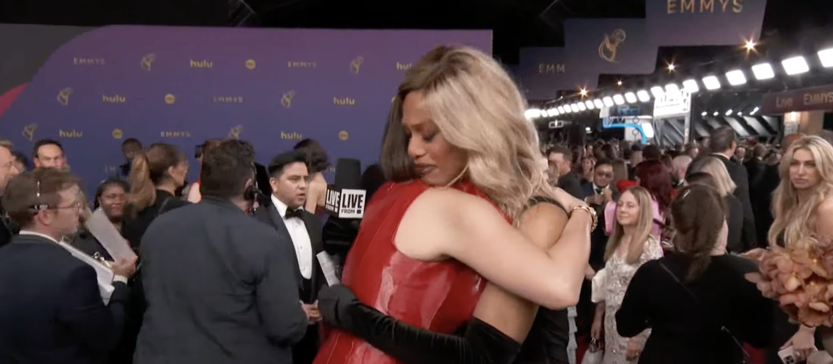 Laverne Cox hugs another person on the red carpet at the Emmys, surrounded by people and reporters
