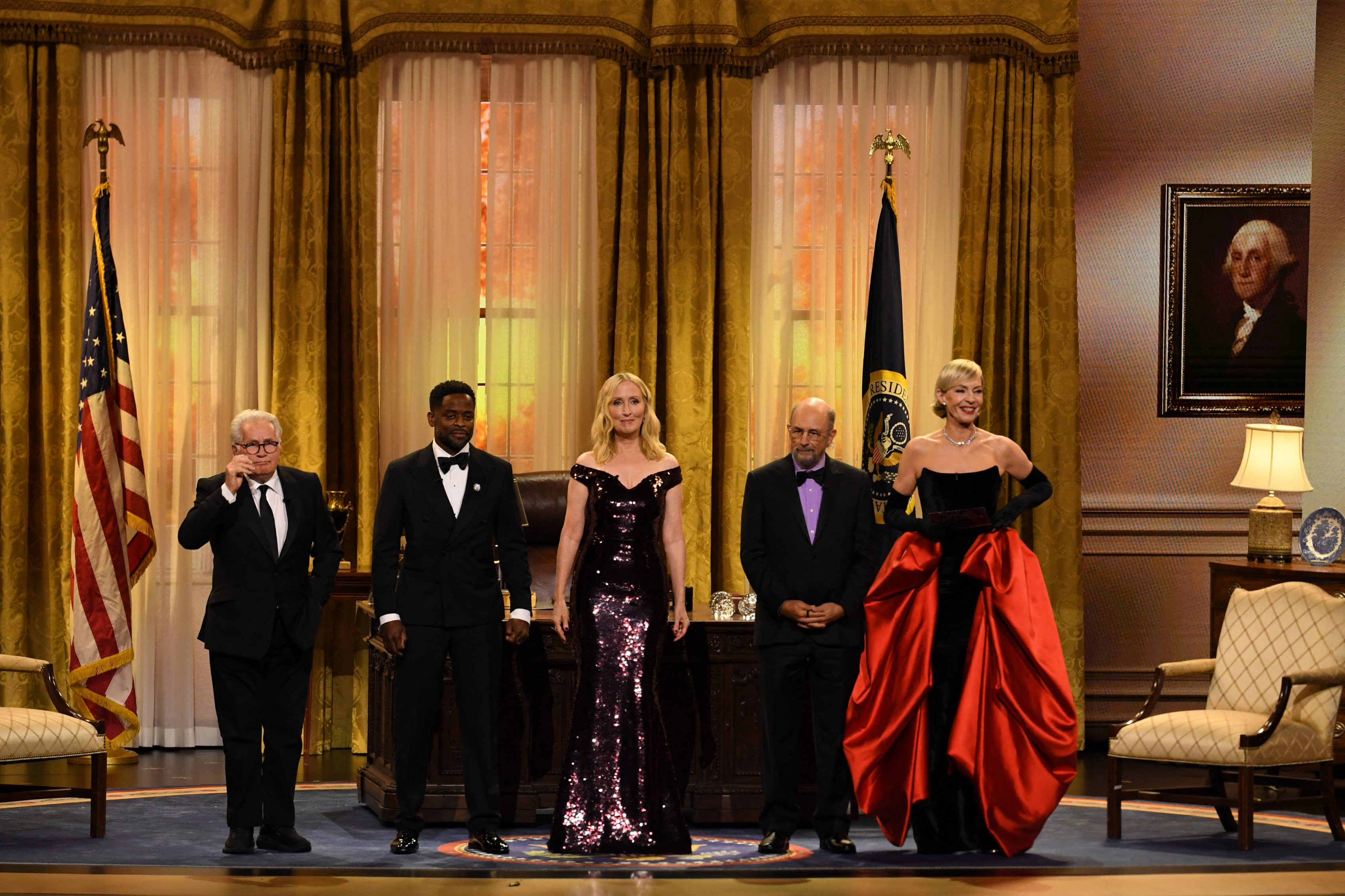 The cast of The West Wing standing on an oval office set on stage