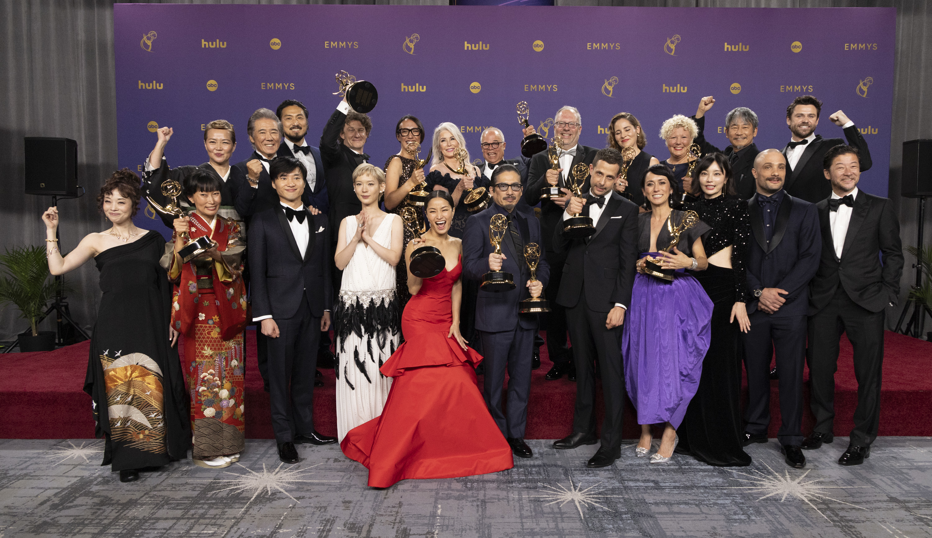The cast and crew of "Shogun" celebrate with their Emmy awards, posing on the red carpet and dressed in various elegant black-tie and formal attire