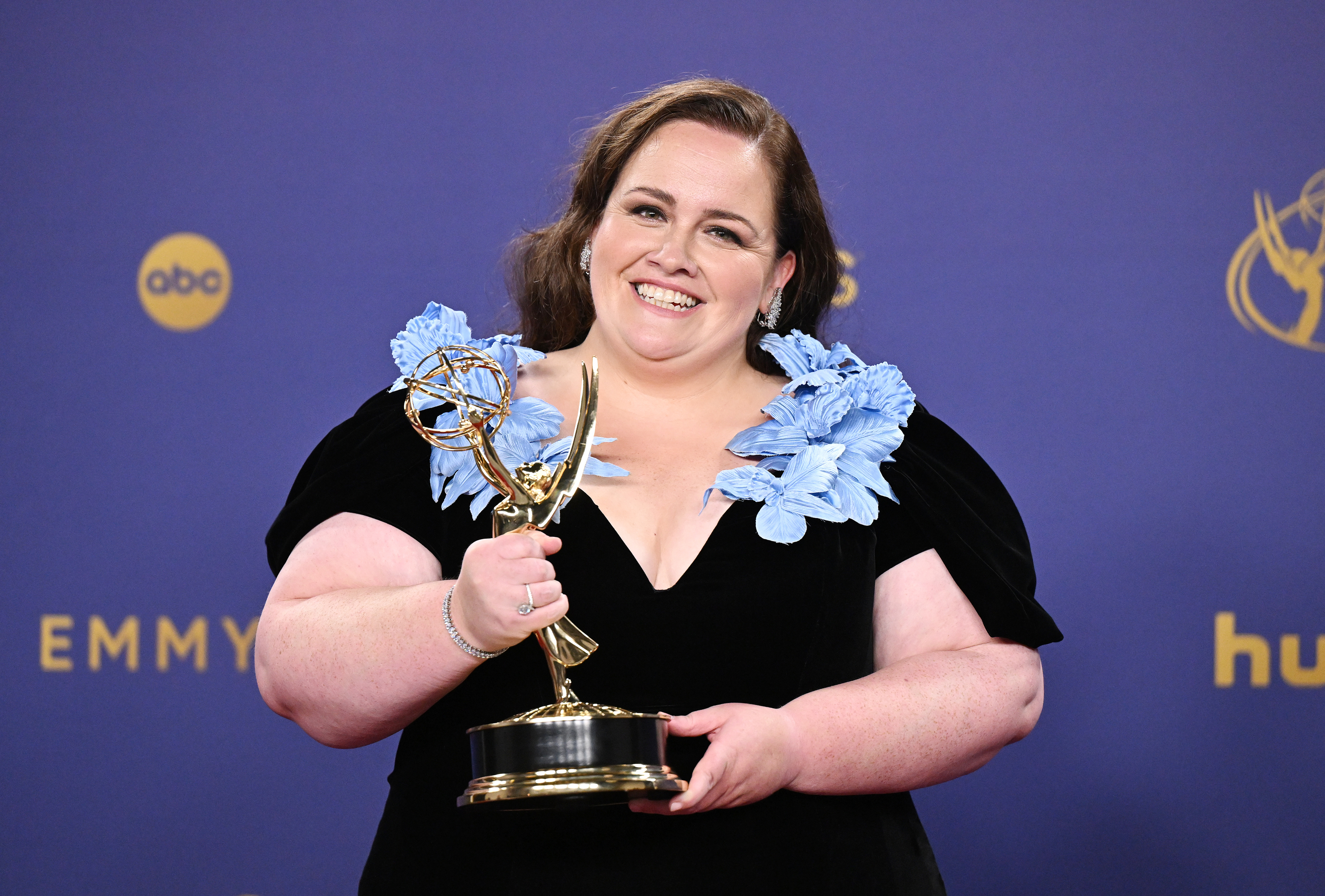 Jessica Gunning holding Emmy award on stage, wearing a black dress with blue floral accents