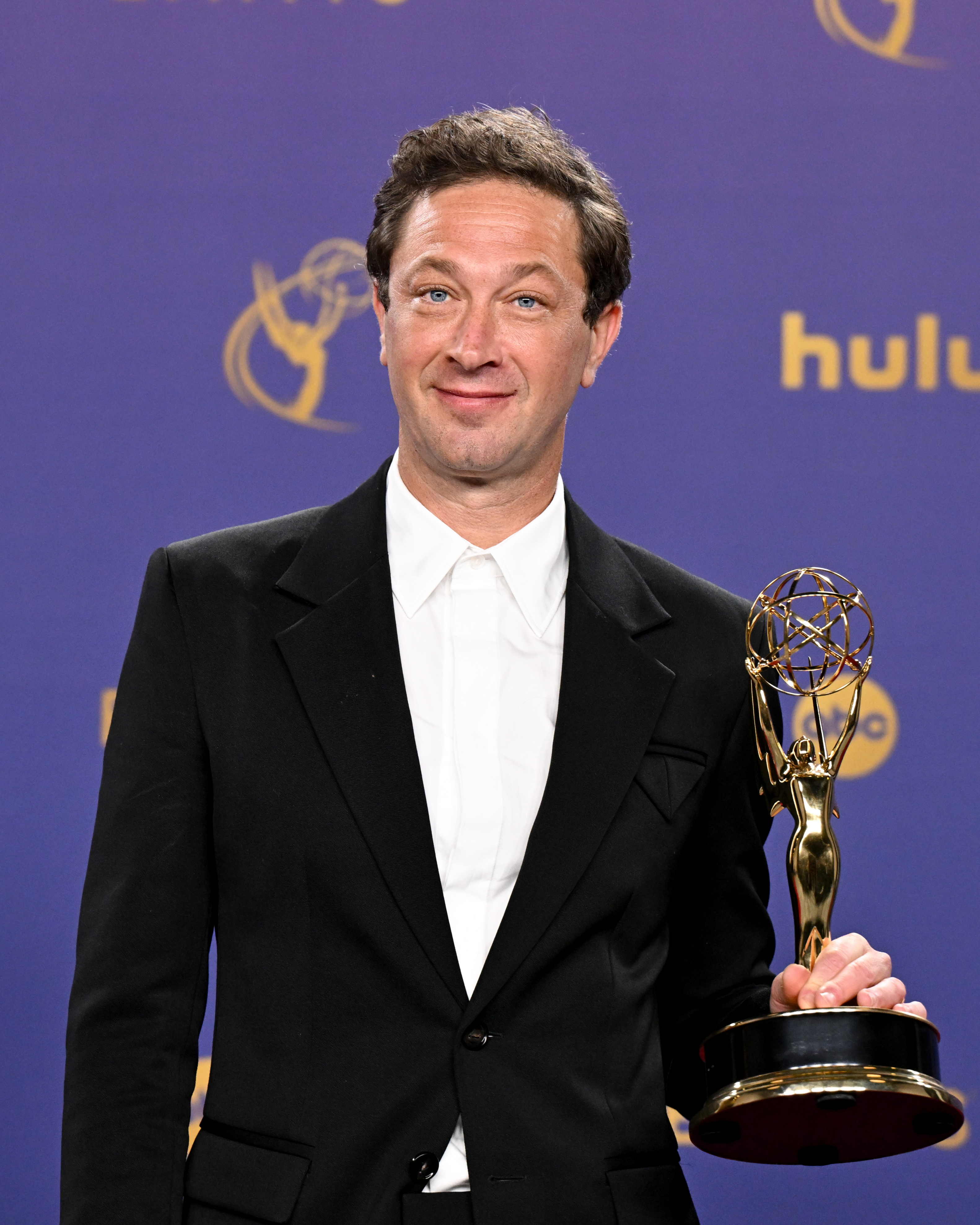 A man in a black suit holds an Emmy award against a Hulu-themed backdrop at an event