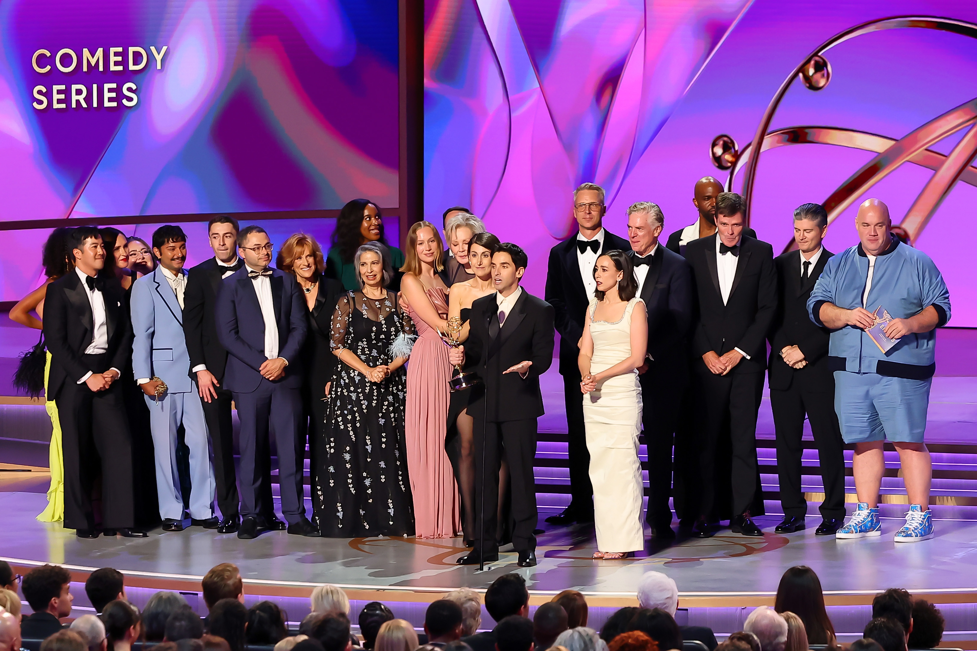 A large cast and crew from Hacks are on stage accepting an award for Comedy Series