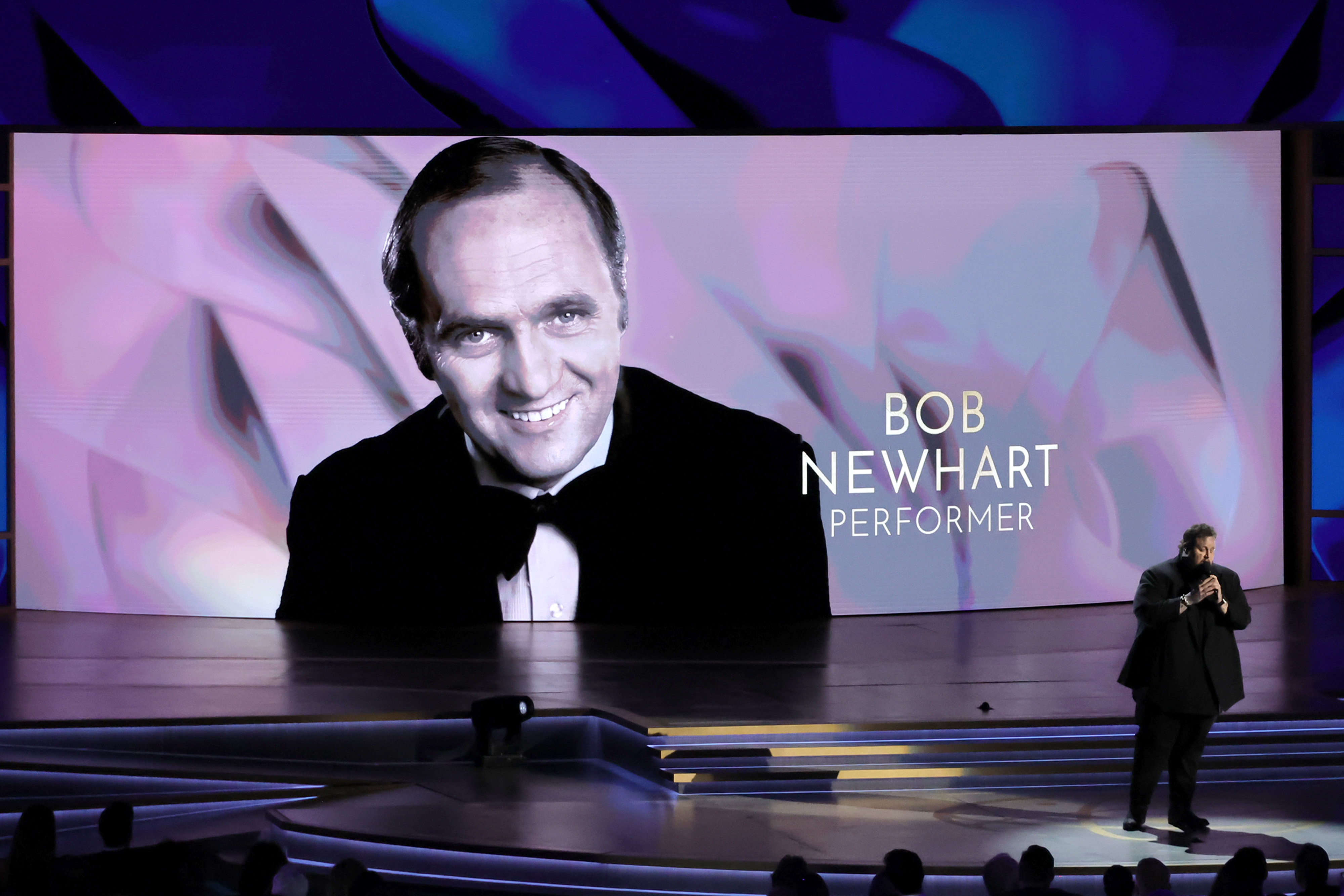 Bob Newhart is honored on stage at an event, shown on a large screen behind with the text "BOB NEWHART PERFORMER."