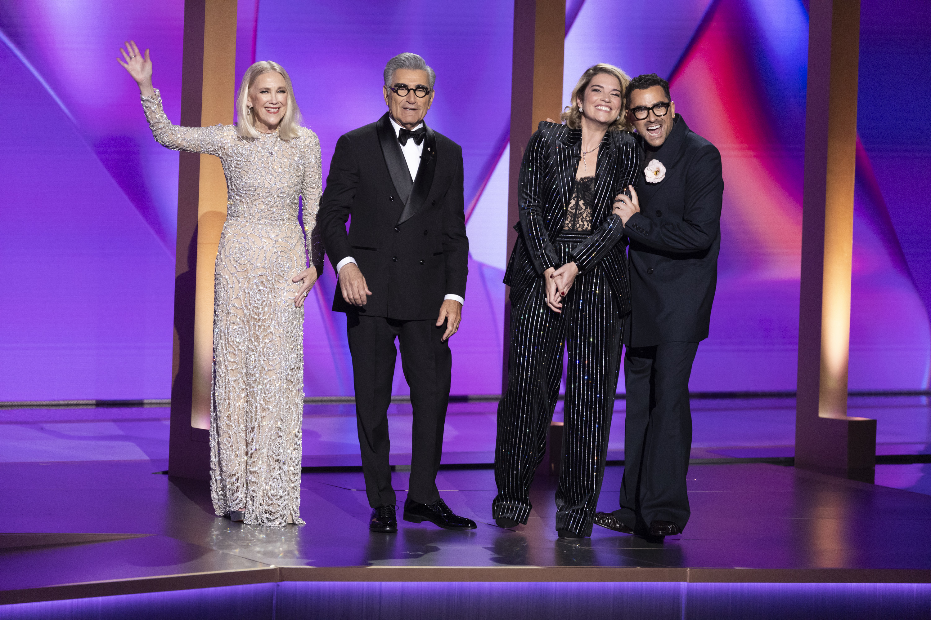 Catherine O'Hara, Eugene Levy, Annie Murphy, and Dan Levy stand on stage. Catherine wears a sequined dress, Eugene and Dan are in tuxedos, and Annie wears a pinstriped suit