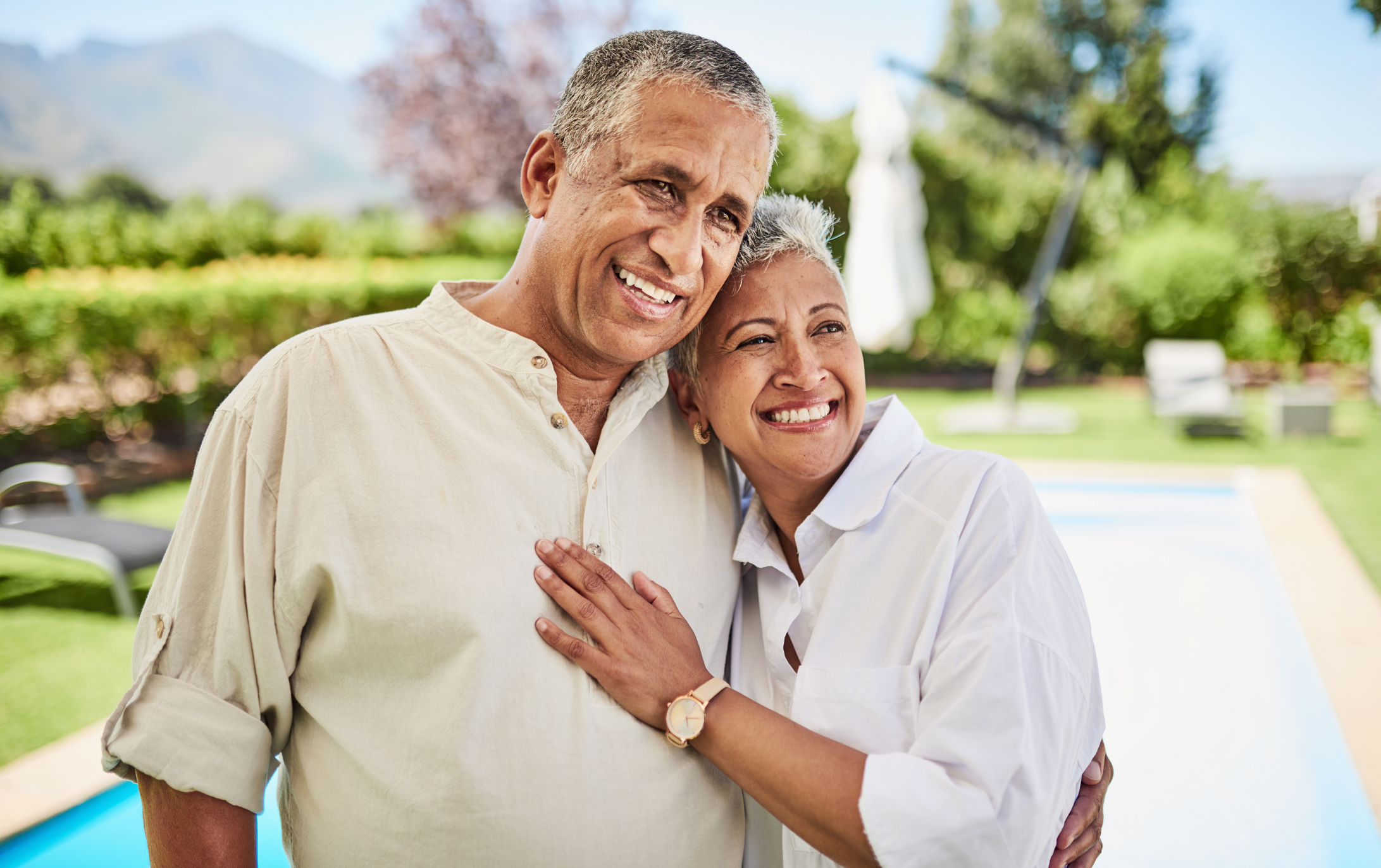 An older couple happily embrace near a pool, smiling warmly at the camera