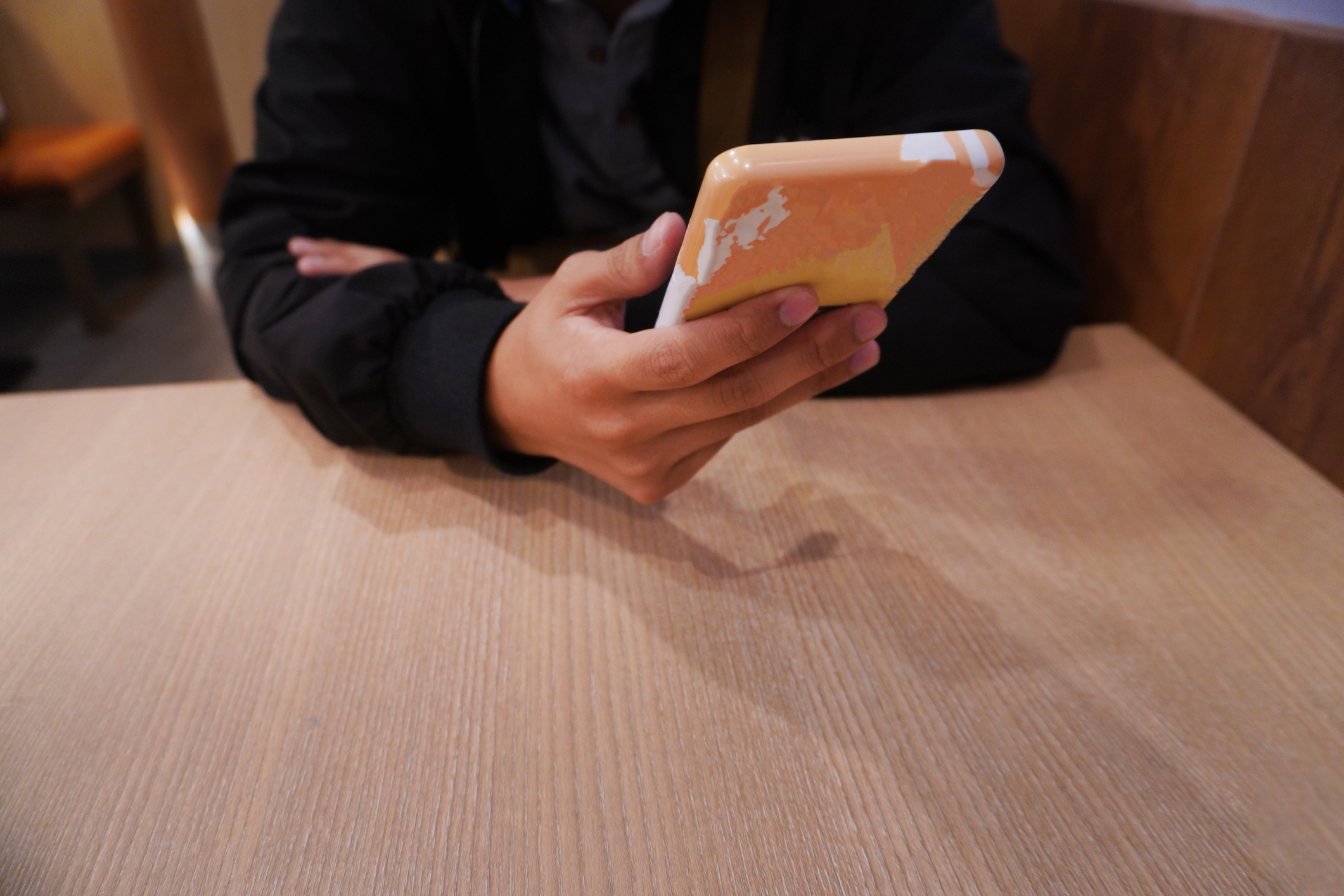 Person sitting at a table holding a smartphone with a patterned case. Face not visible