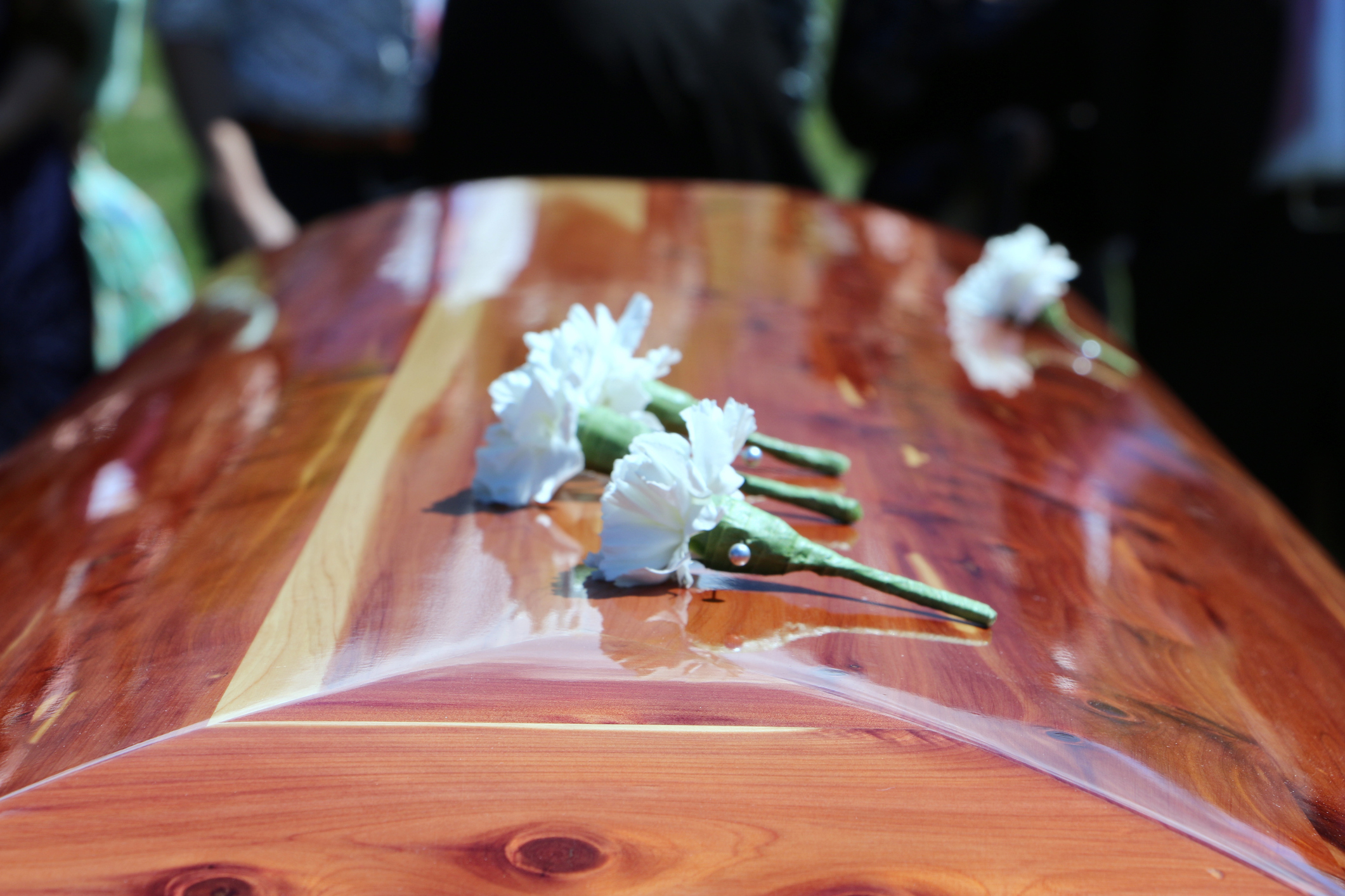 A wooden casket with white flowers placed on top, surrounded by people in mourning