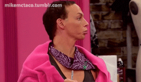 A person in a pink robe with a purple bandana assesses something off-screen, sitting and holding a pen in a gym-like setting. Signature in the top left