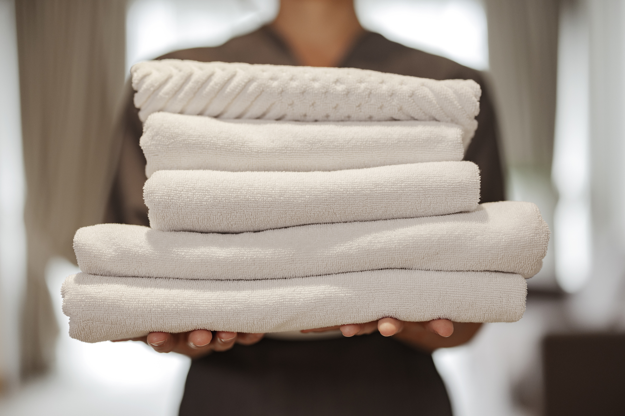 A person holding a neatly stacked set of clean, rolled towels in a luxurious hotel setting