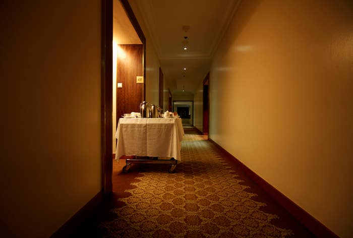 A hotel corridor with dim lighting and a cart filled with food and beverages placed near one of the doors