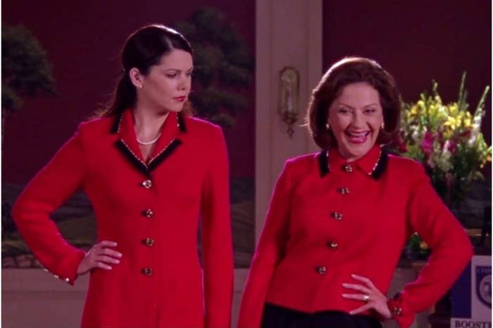 Lauren Graham and Kelly Bishop in red suits, standing next to each other; one looks puzzled, the other is laughing, likely in a scene from &quot;Gilmore Girls.&quot;