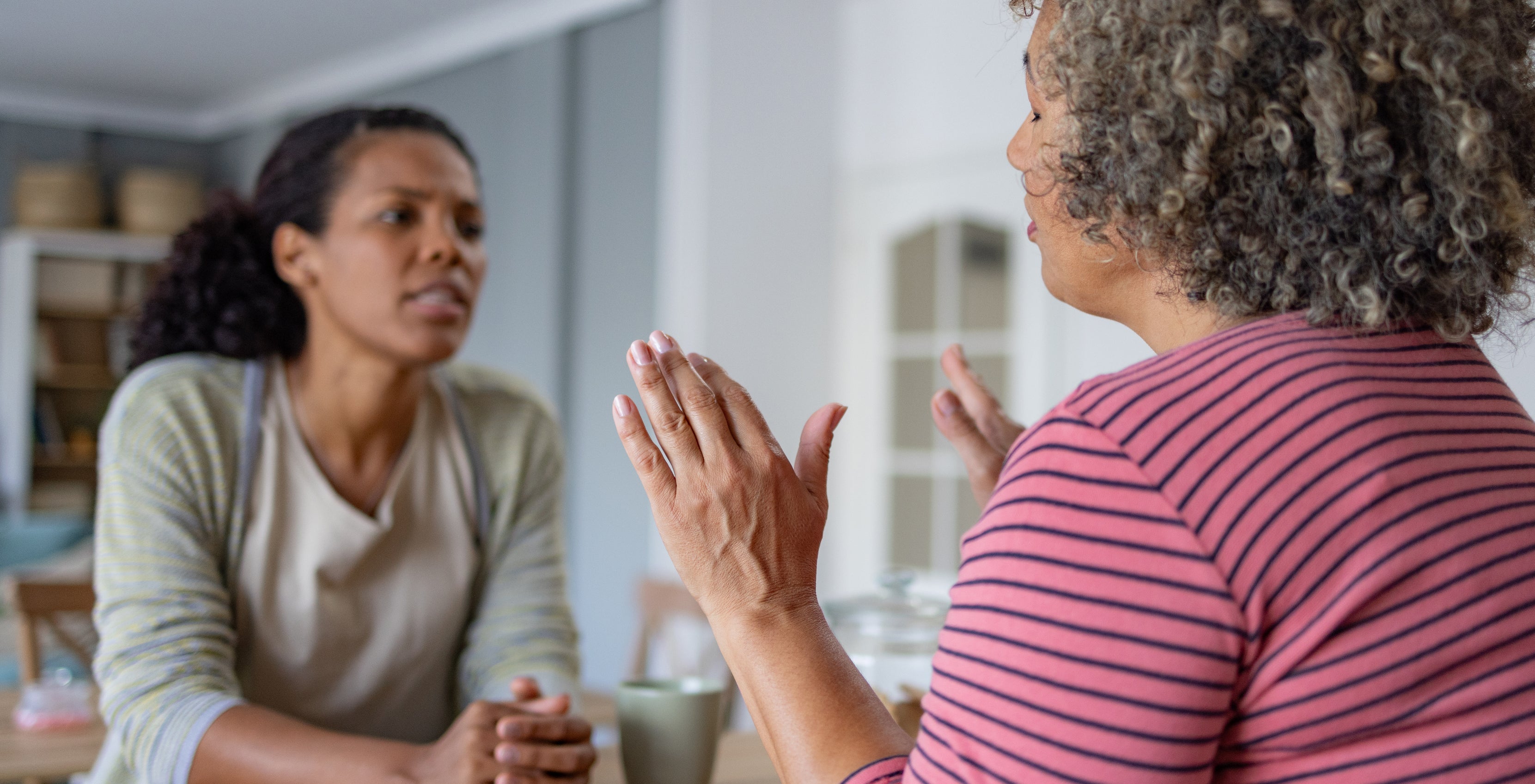 Two women are sitting at a table, engaged in a serious conversation. One woman is gesturing with her hands while the other listens attentively