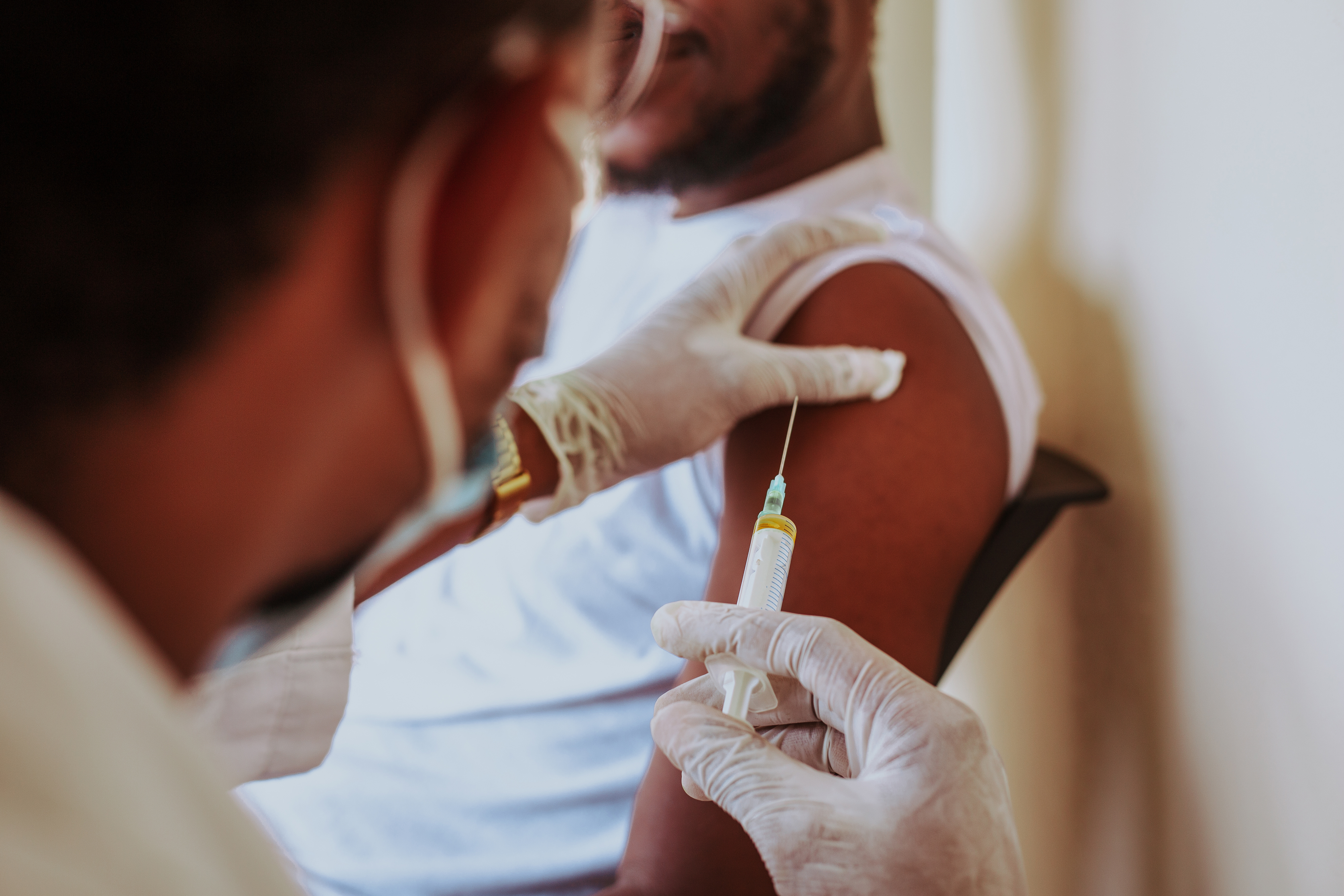 A healthcare worker administers a vaccine to a seated person who wears a sleeveless shirt