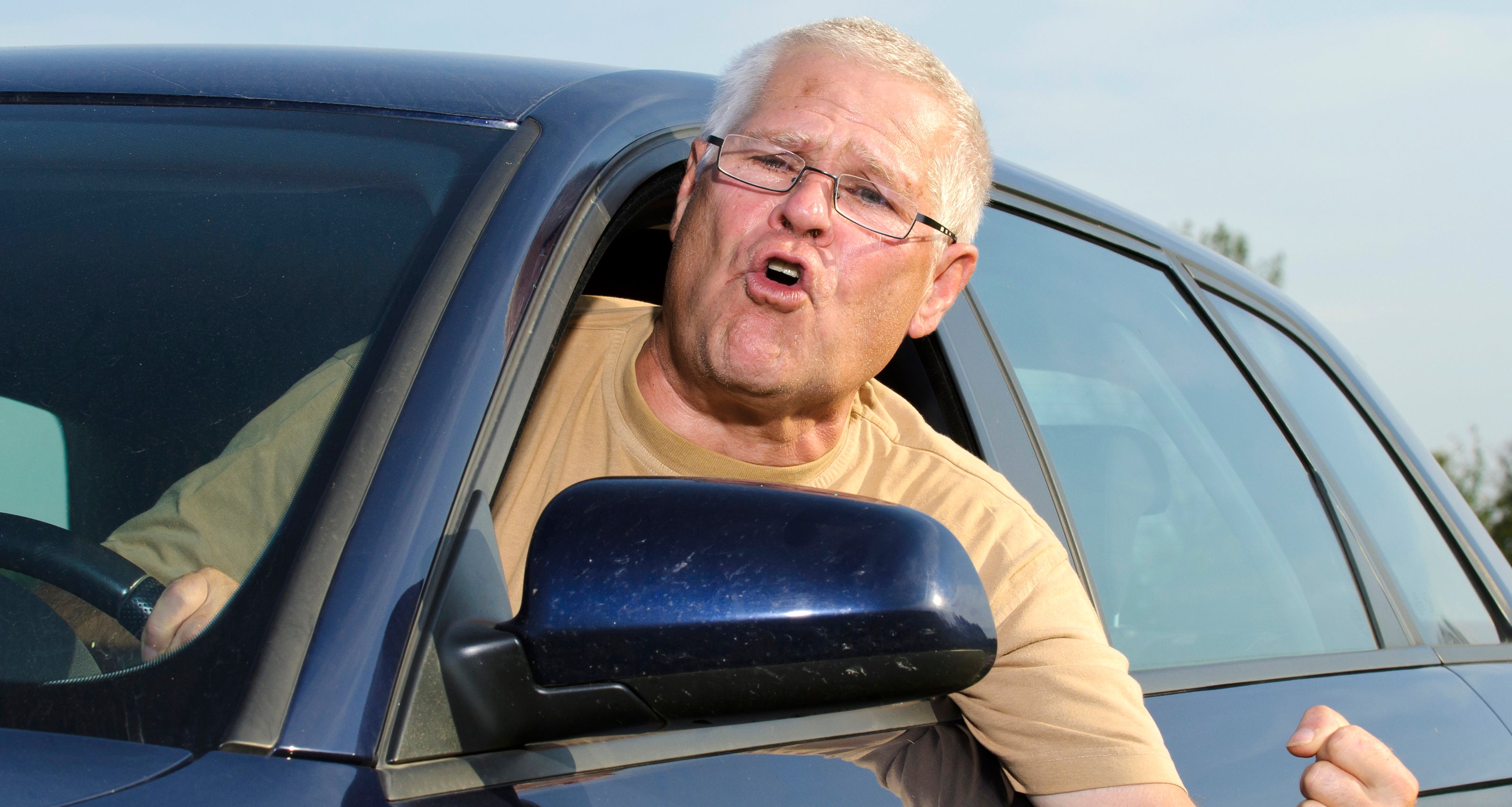 A man leans out of his car window, appearing angry and shaking his fist