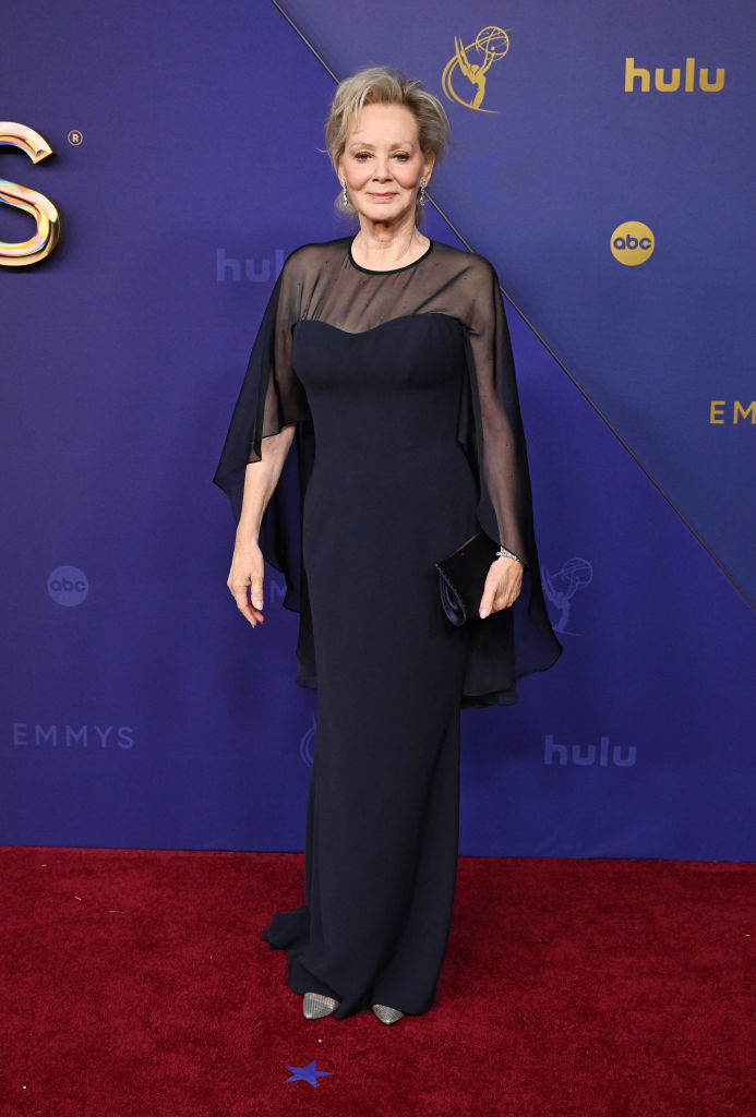 Jean Smart on the red carpet at the Emmys, wearing a flowing, elegant black gown with sheer cape sleeves