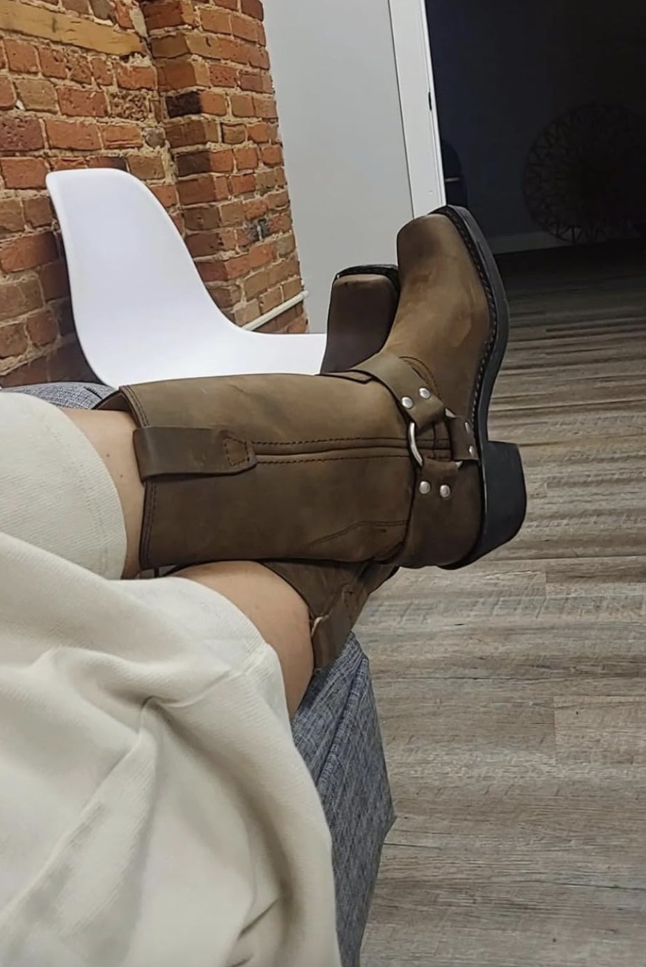 Person relaxing with legs up, wearing tan boots. Background includes a achromatic  seat  and ceramic  wall