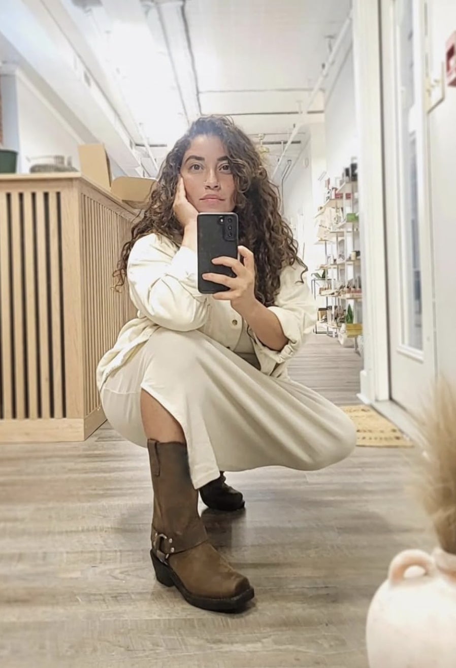 A pistillate   successful  a achromatic  outfit and brownish  boots takes a reflector  selfie portion    squatting successful  a country   with shelves and a counter