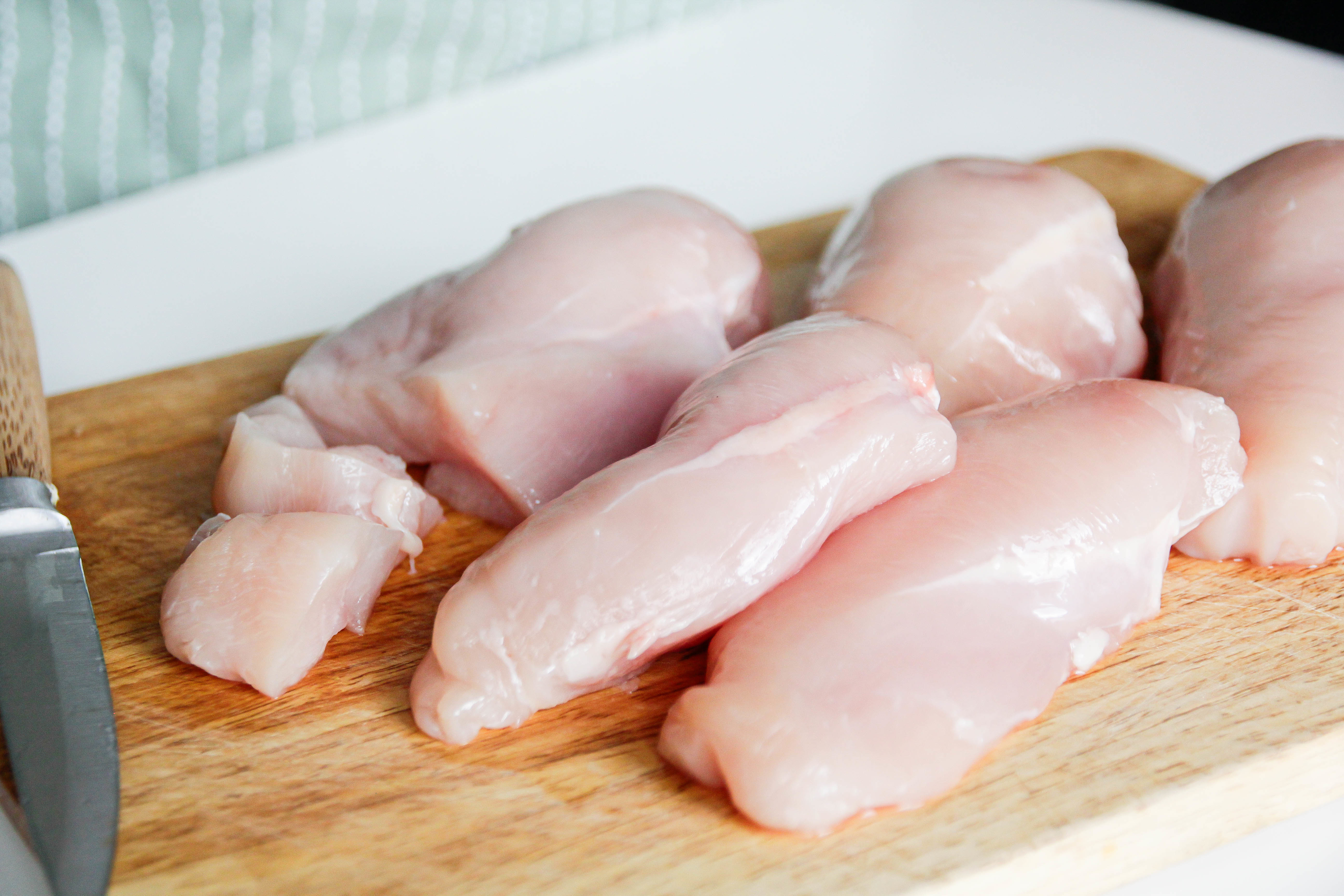 Raw chicken breasts and a knife on a wooden cutting board