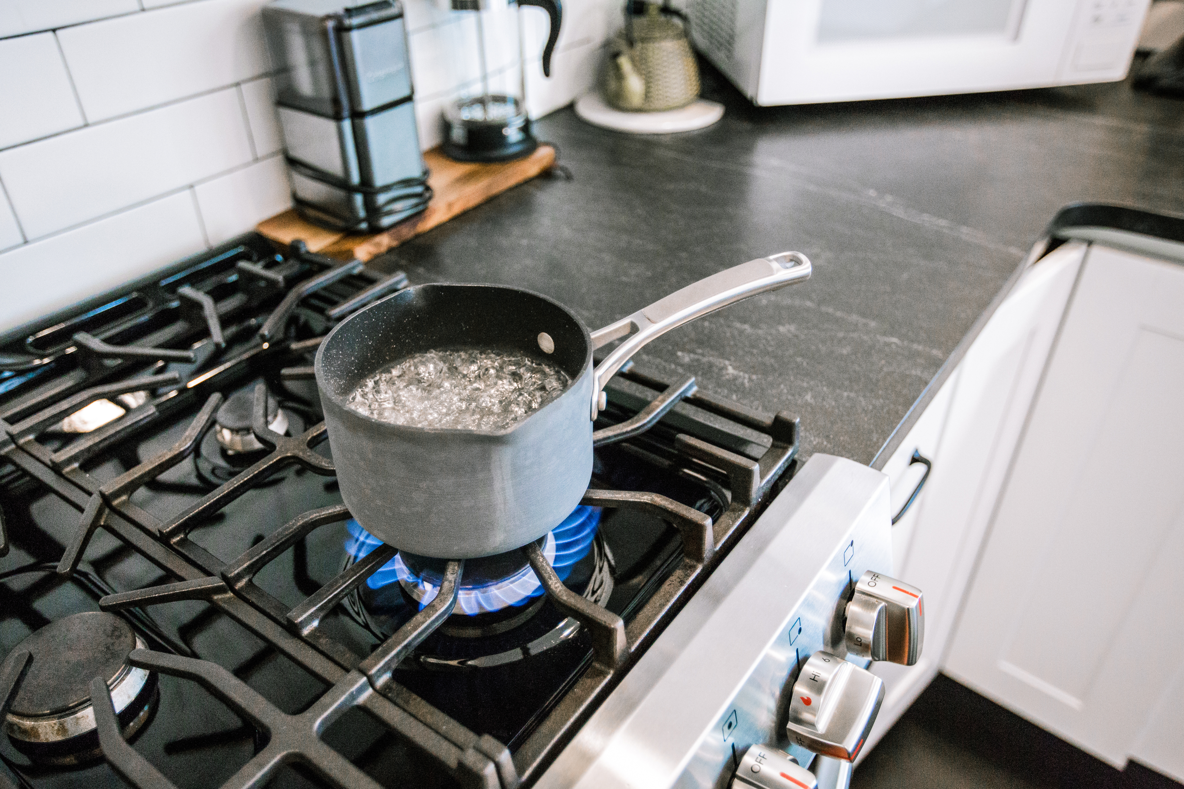 A pot of water boiling on a modern gas stove in a kitchen, surrounded by typical kitchen appliances and utensils