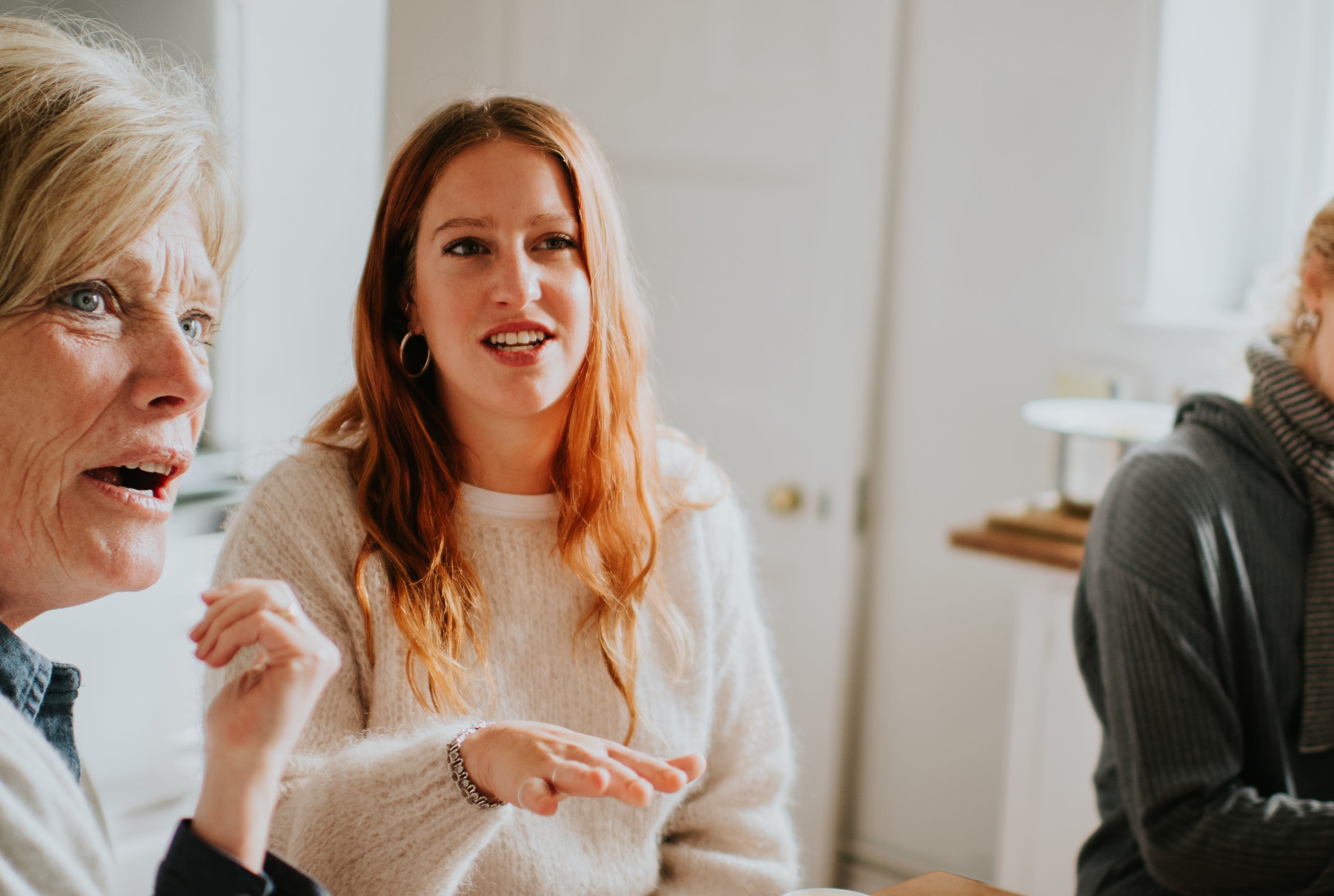 Four people converse around a wooden table with food and drinks, appearing engaged and animated in discussion.