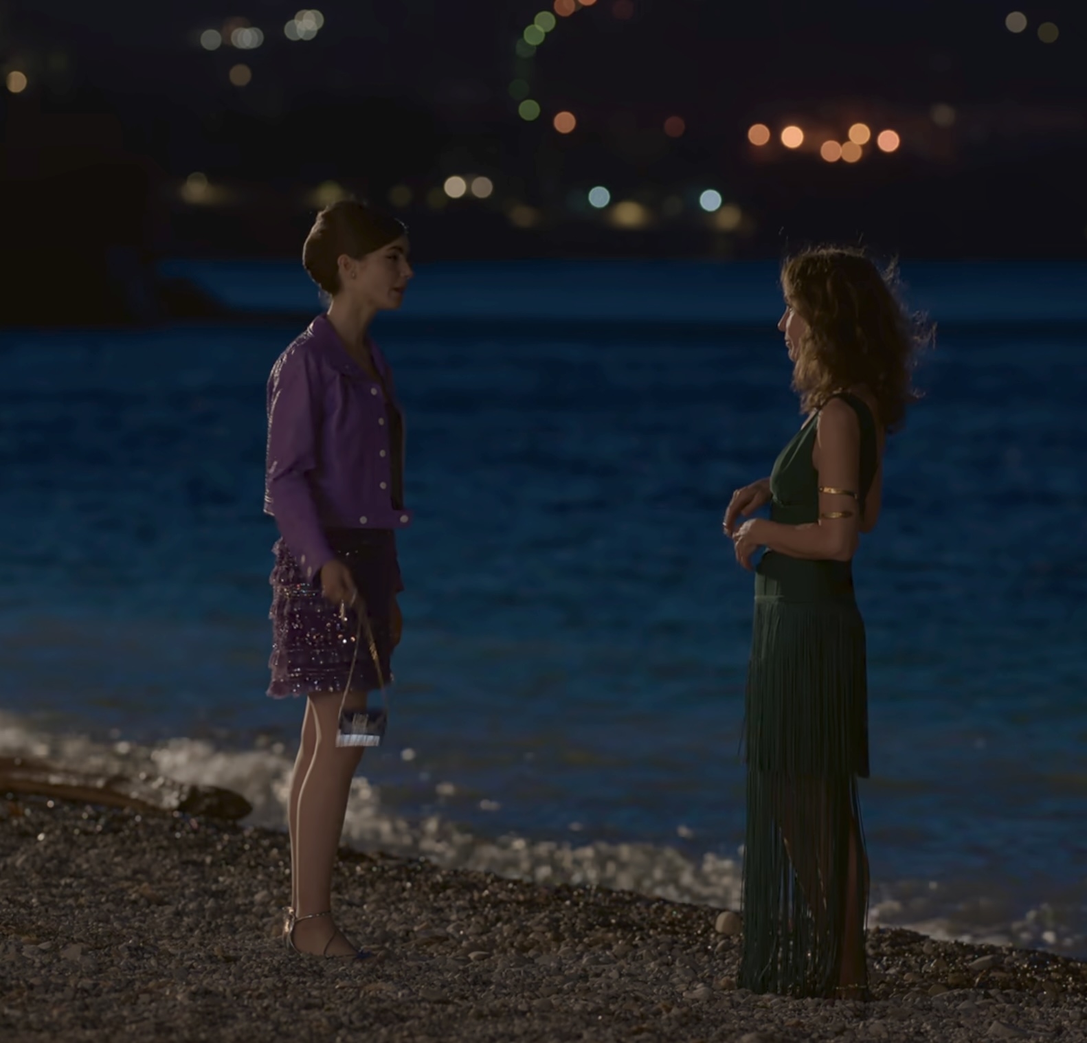 Lily Collins and Philippine Leroy-Beaulieu  talking on a beach at night. Lily wears a stylish sequined outfit and Phillippine wears an elegant fringed dress