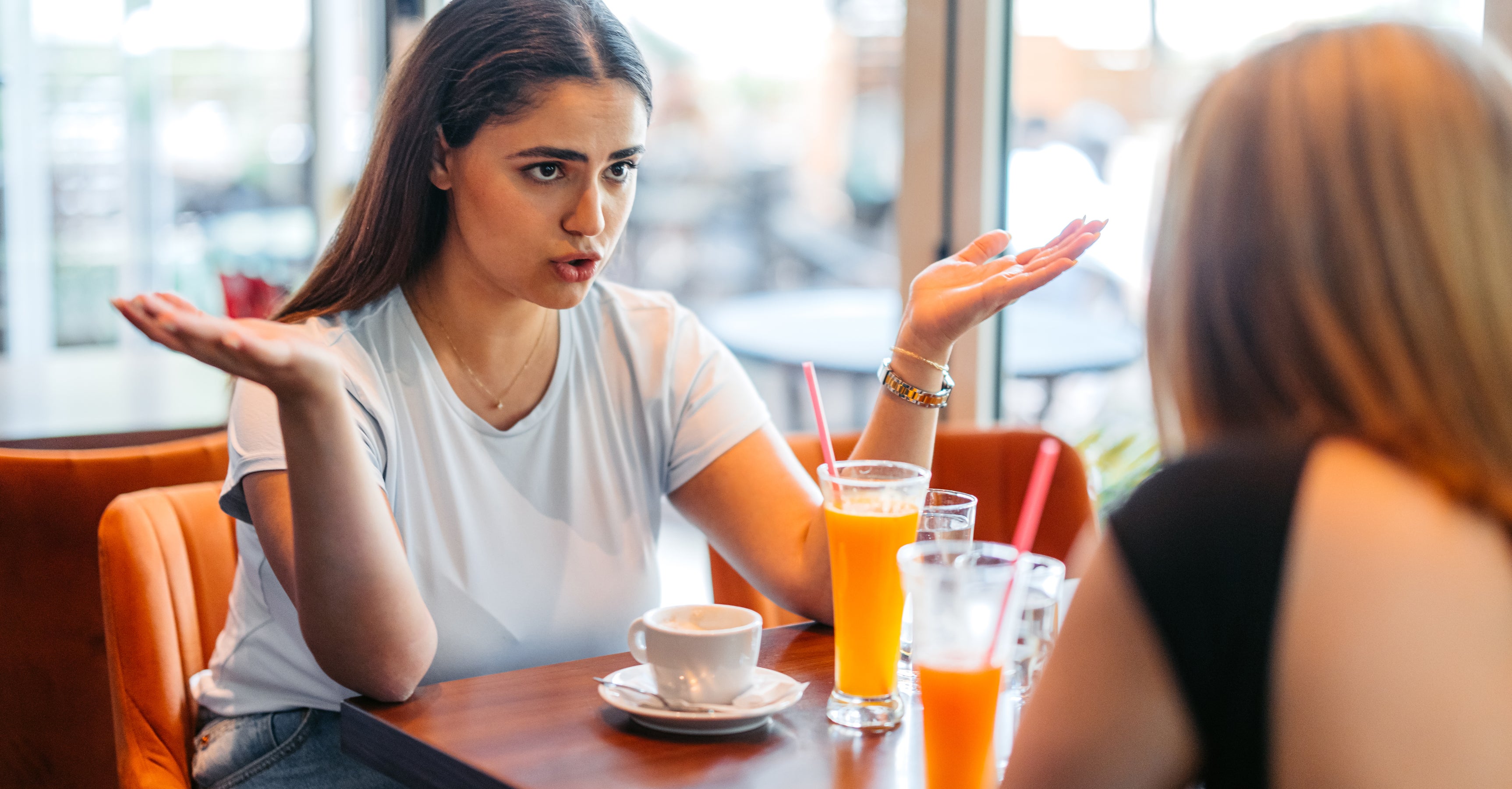 Two women engaged in a conversation at a cafe, one with an expressive gesture