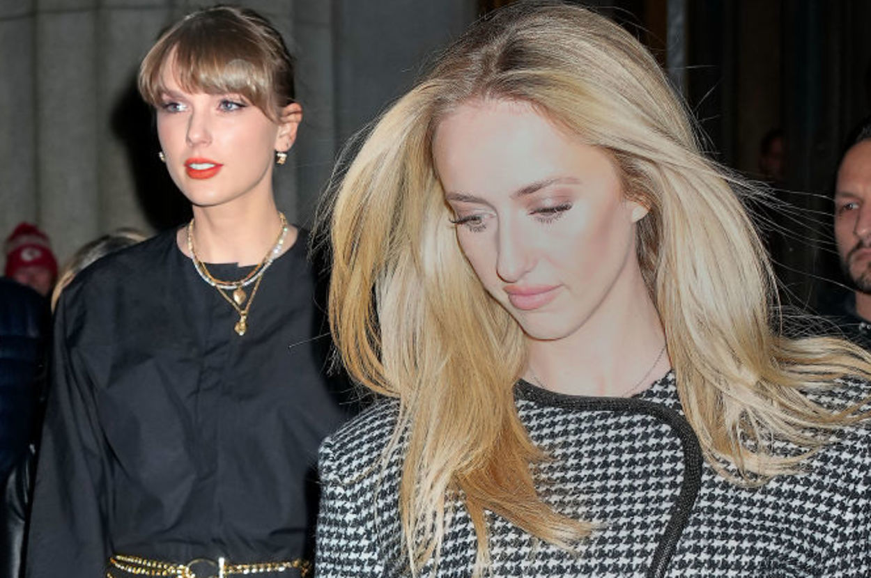 Taylor Swift and a friend are walking outside, Swift is dressed in a black outfit with tights and a gold chain belt