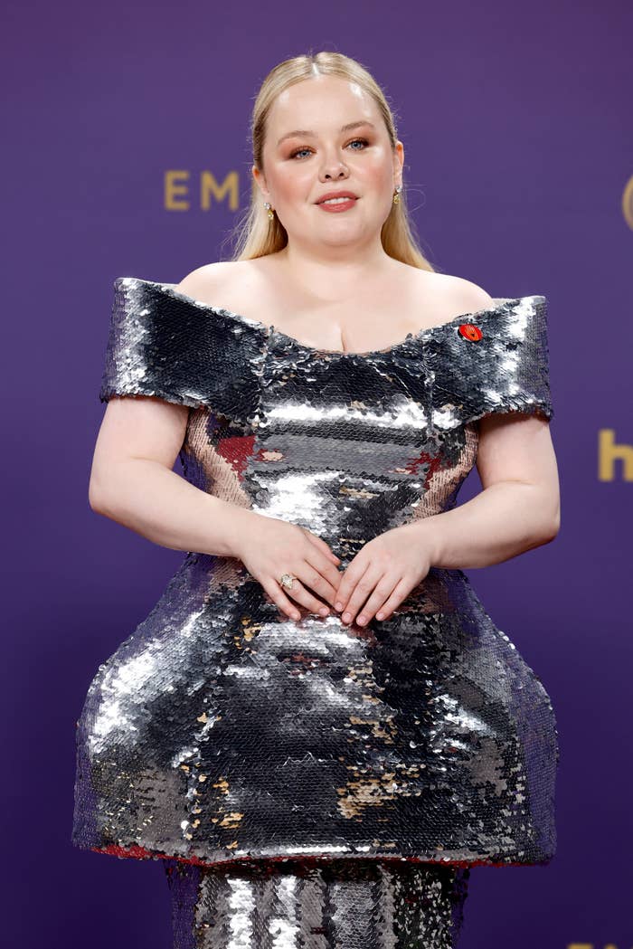 Nicola Coughlan wears a metallic, structured off-shoulder gown, posing on the red carpet