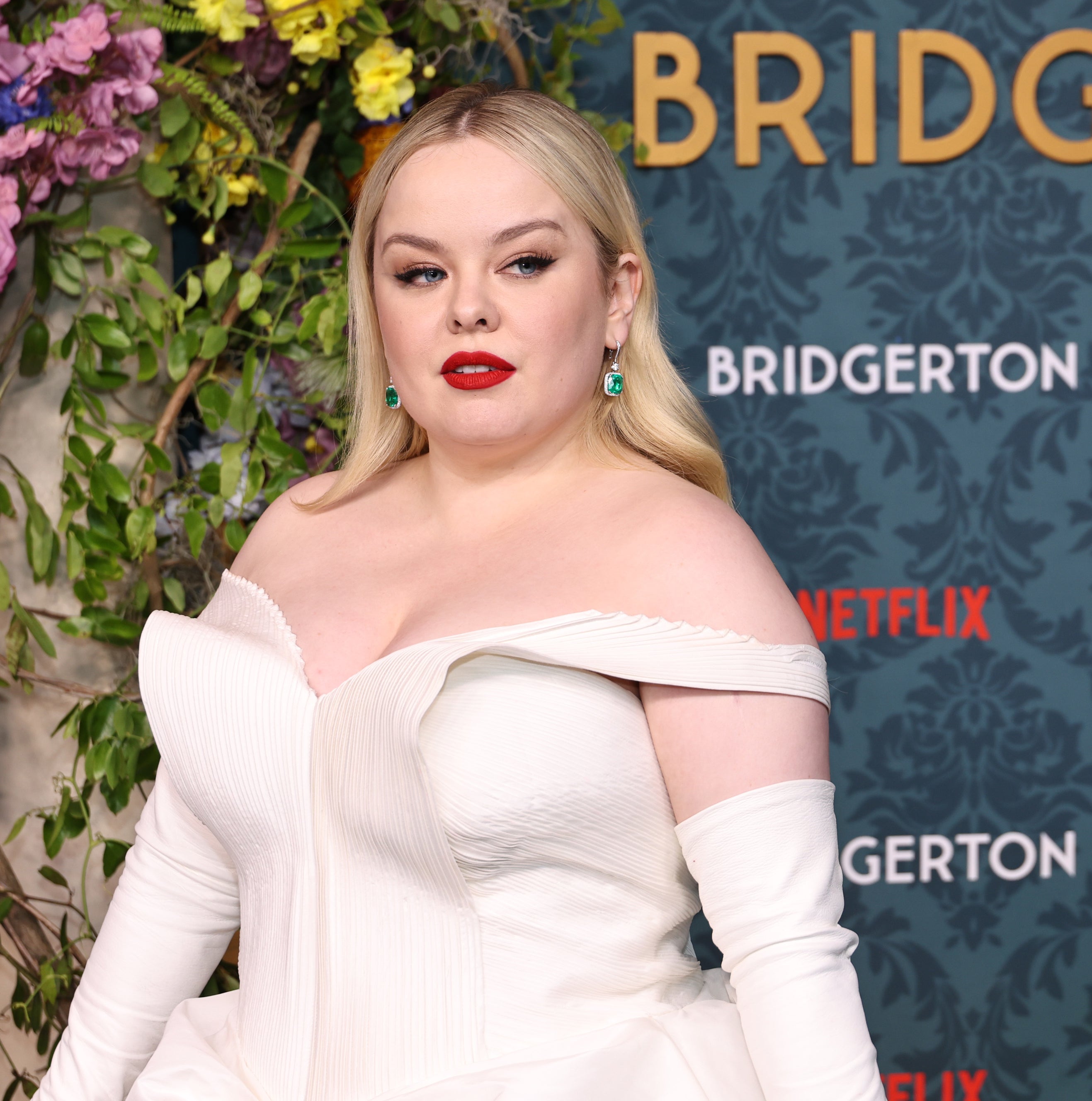 Nicola Coughlan at the &quot;Bridgerton&quot; event, wearing an off-the-shoulder gown, standing in front of a floral and themed backdrop