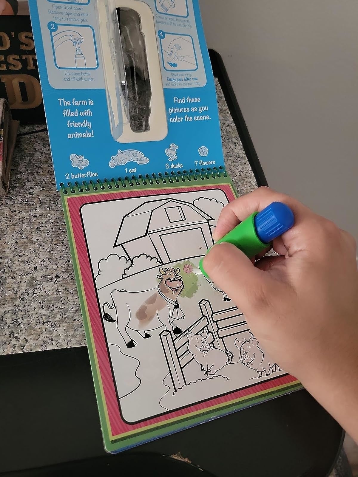 Hand utilizing a greenish  marker to colour  barn animals connected  a farm-themed children's coloring book