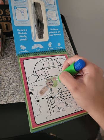 Hand utilizing a greenish marker to colour barn animals connected a farm-themed children's coloring book