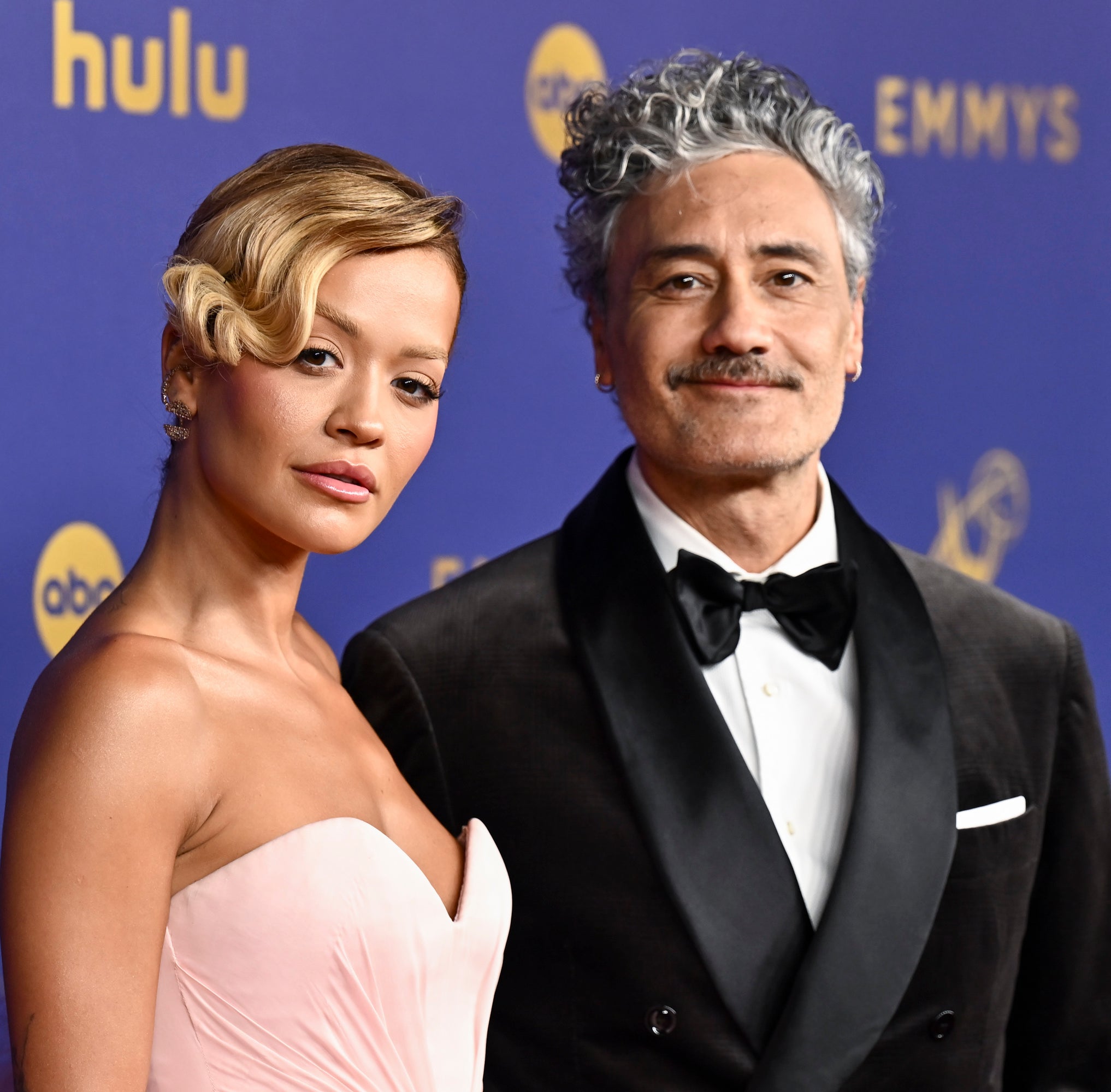 Rita Ora in a strapless dress and Taika Waititi in a tuxedo pose together on the red carpet at the Emmy Awards