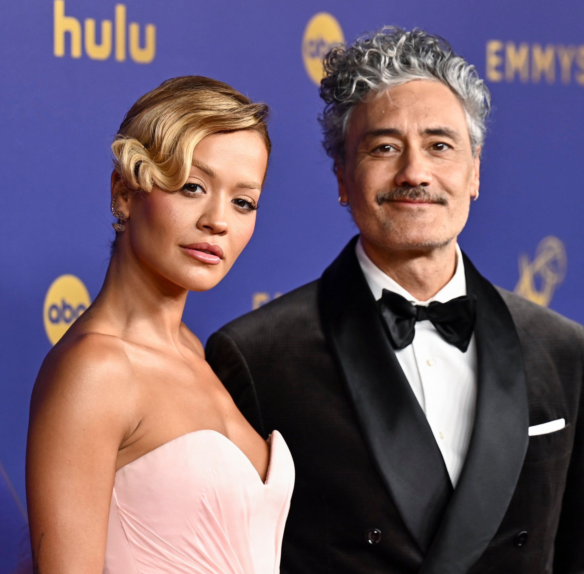 Rita Ora in a strapless dress and Taika Waititi in a tuxedo pose together on the red carpet at the Emmy Awards