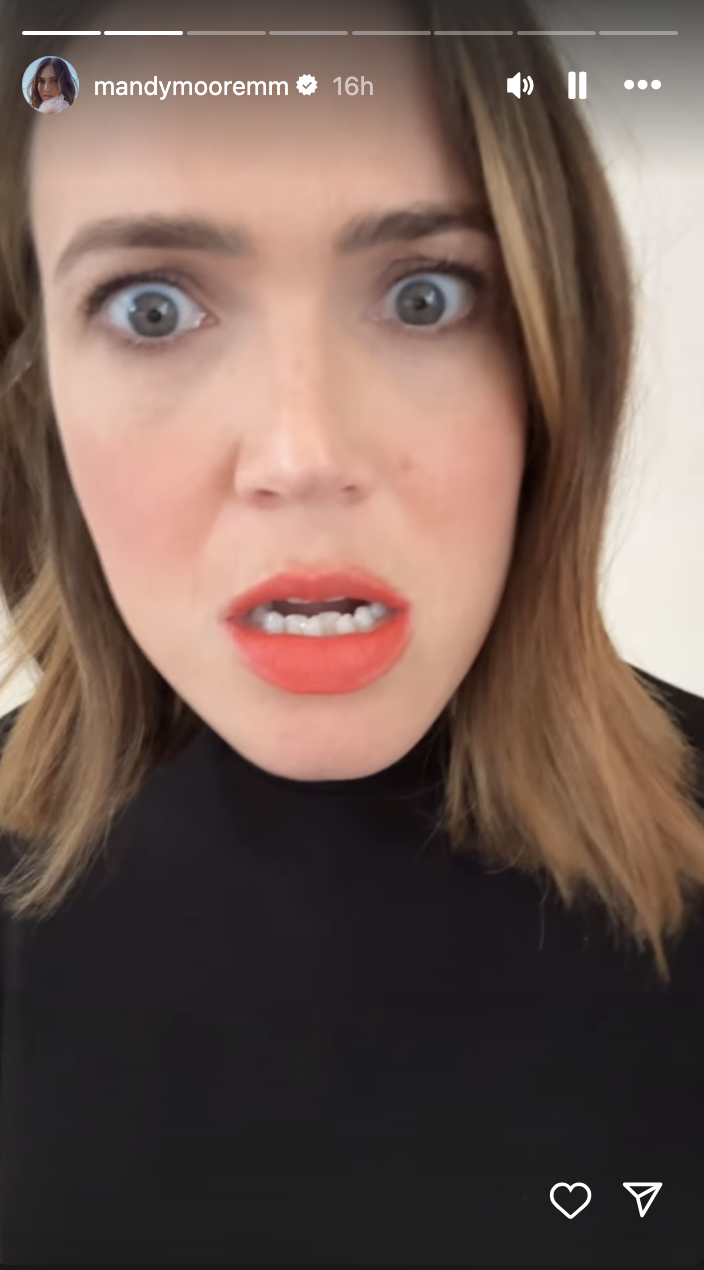 Mandy Moore, with wide-eyed expression and bright red lipstick, wearing a high-neck top