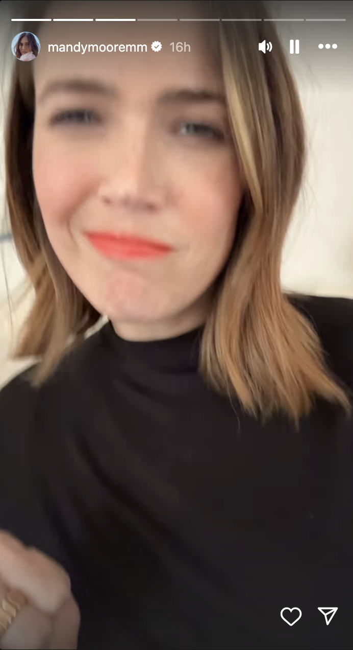 Mandy Moore takes a selfie wearing a high-neck, long-sleeve top, and light makeup while smiling slightly. Instagram story timestamp reads "16h"